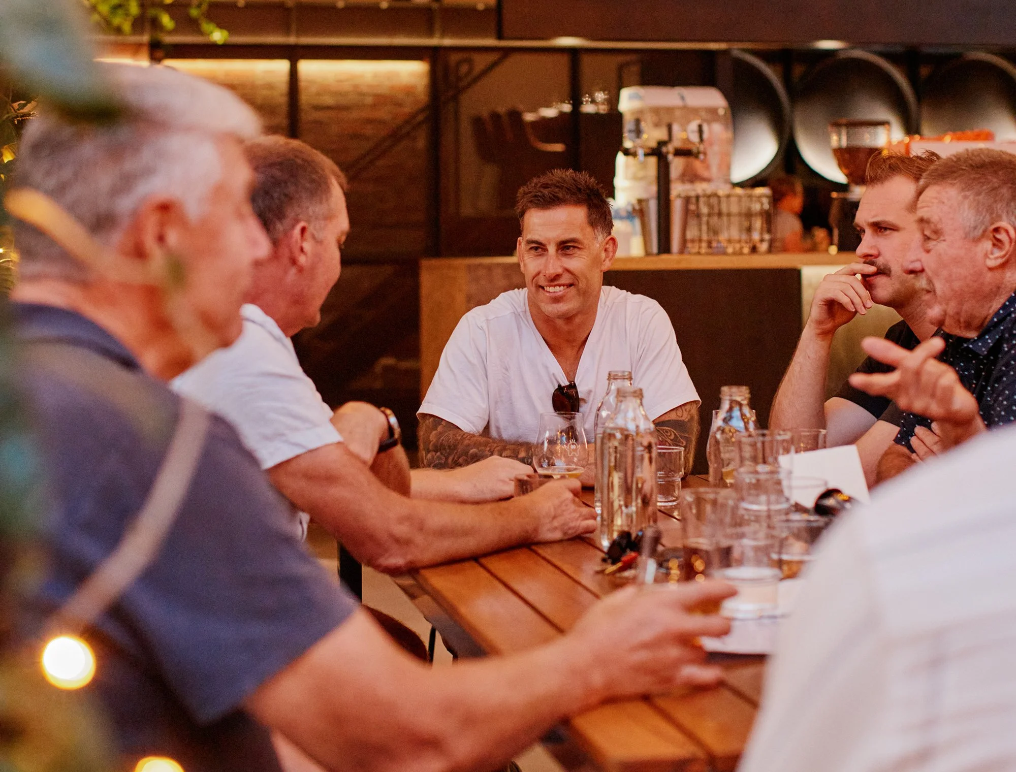 A group of men sitting around a wooden table having a conversation at a restaurant.