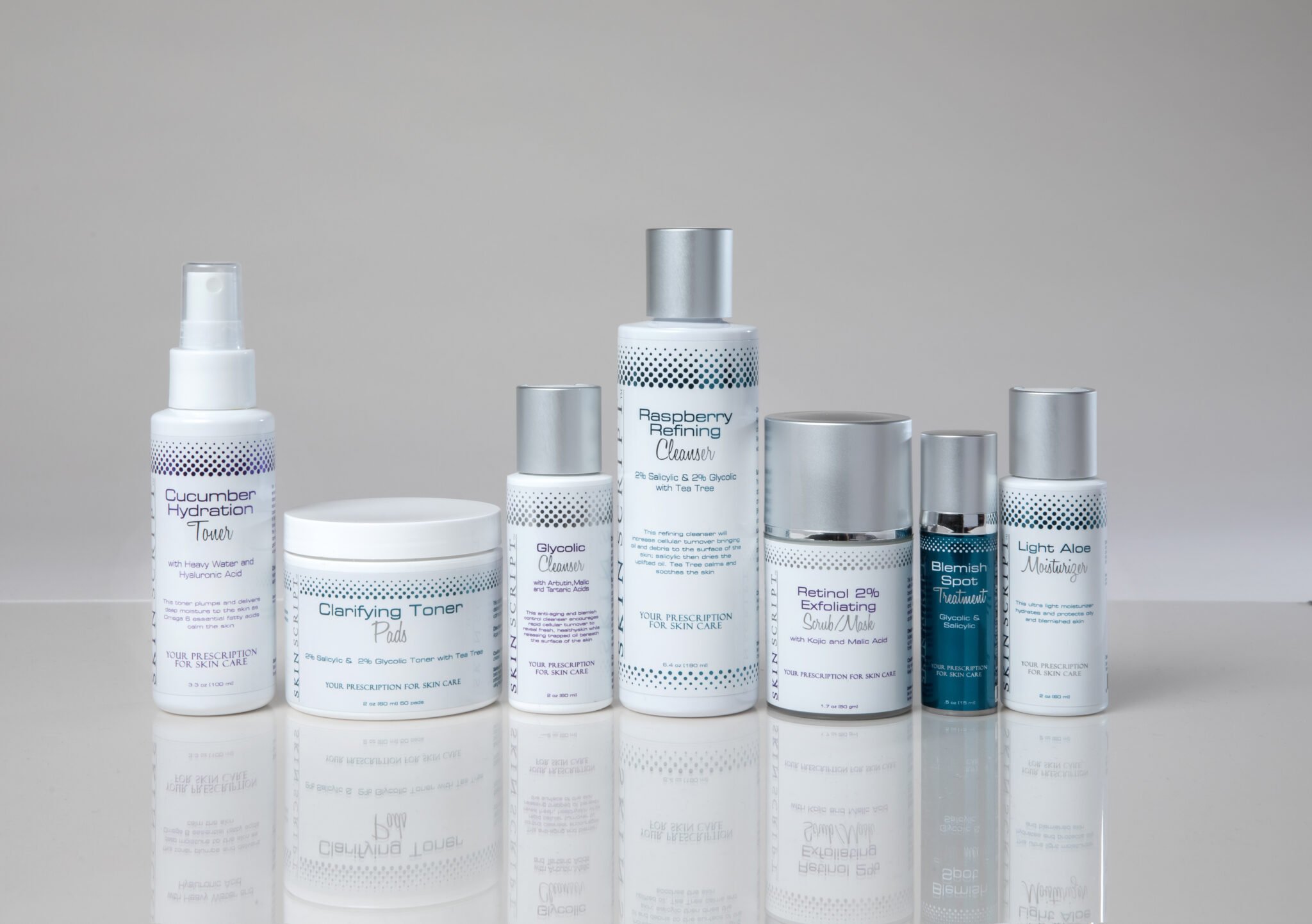 Collection of skincare products including cucumber hydration toner, clarifying toner pad, glycolic cleanser, raspberry refining cleanser, retinol exfoliating scrub mask, blemish spot treatment, and light aloe moisturizer, arranged on reflective surface.