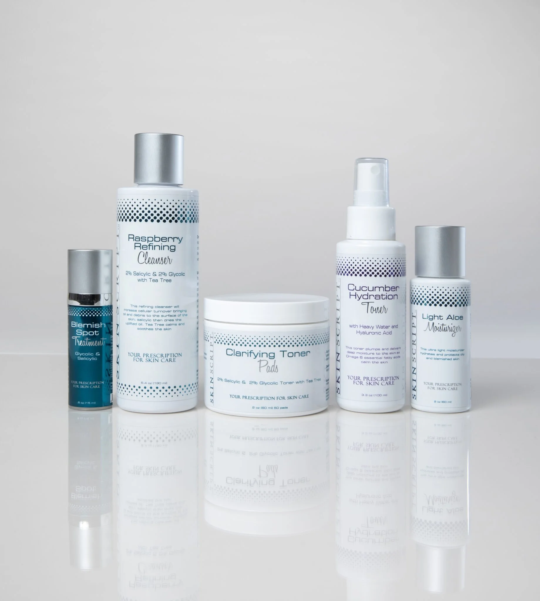 A collection of skincare products including a Blemish Spot Treatment, Raspberry Refining Cleanser, Clarifying Toner Pads, Cucumber Hydration Toner, and Light Aloe Moisturizer, displayed on a reflective surface against a plain gray background.