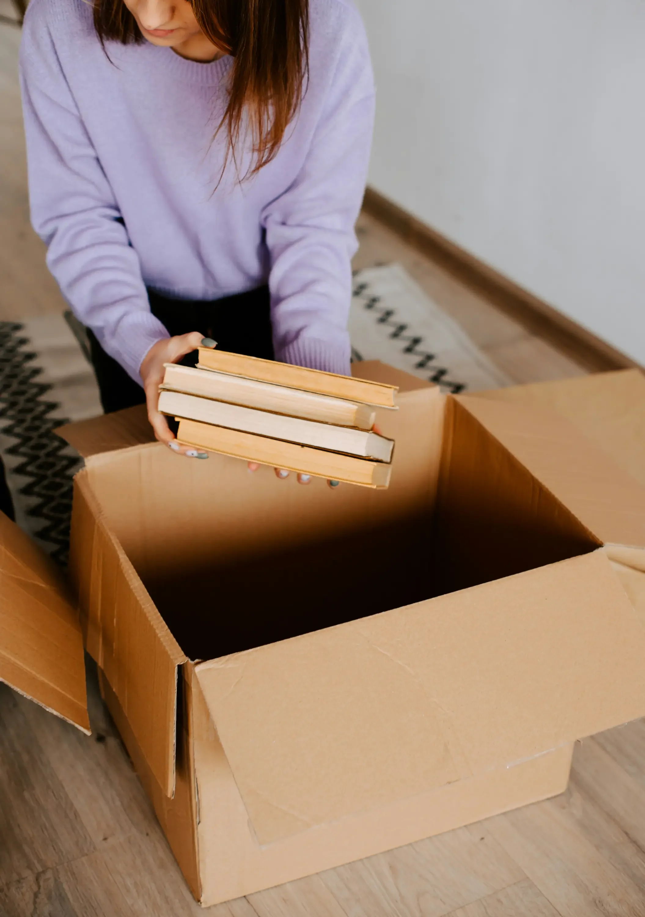 a woman in a lavendar sweater placing books in an empty moving box before her move out clean service