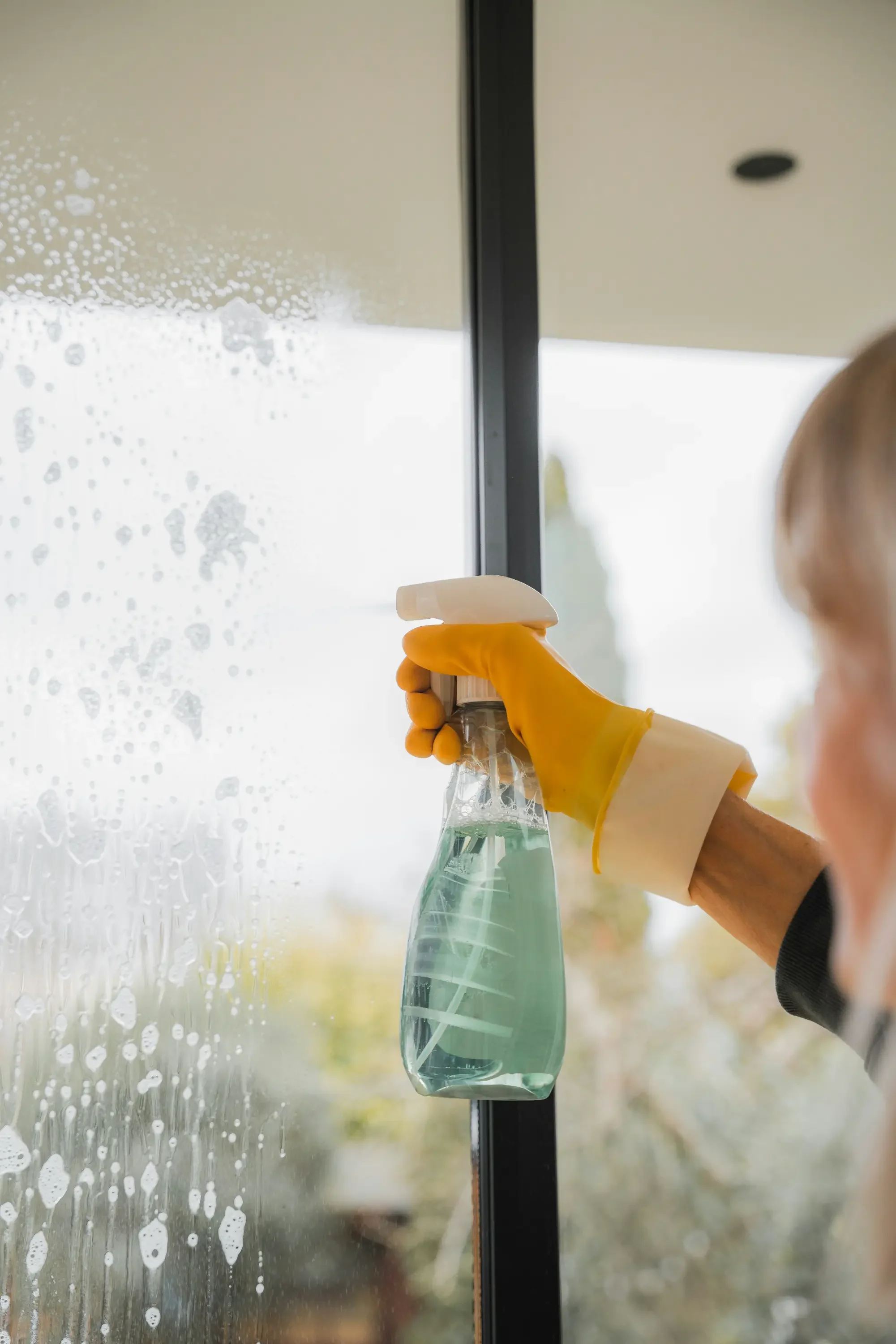 Professional cleaner removing construction residue and overspray from a glass window — post-construction cleaning service by My Favorite Cleaning Co.