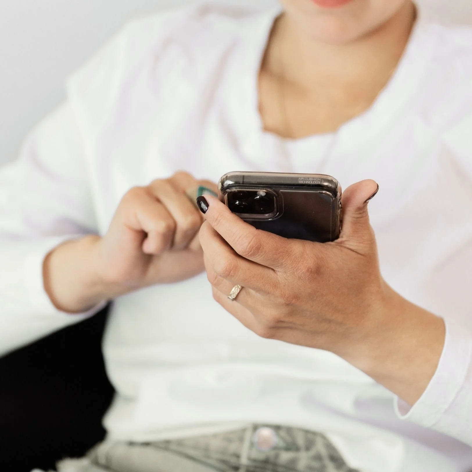 woman in a white shirt with dark fingernail polish, holding a phone as if to answer a phone call