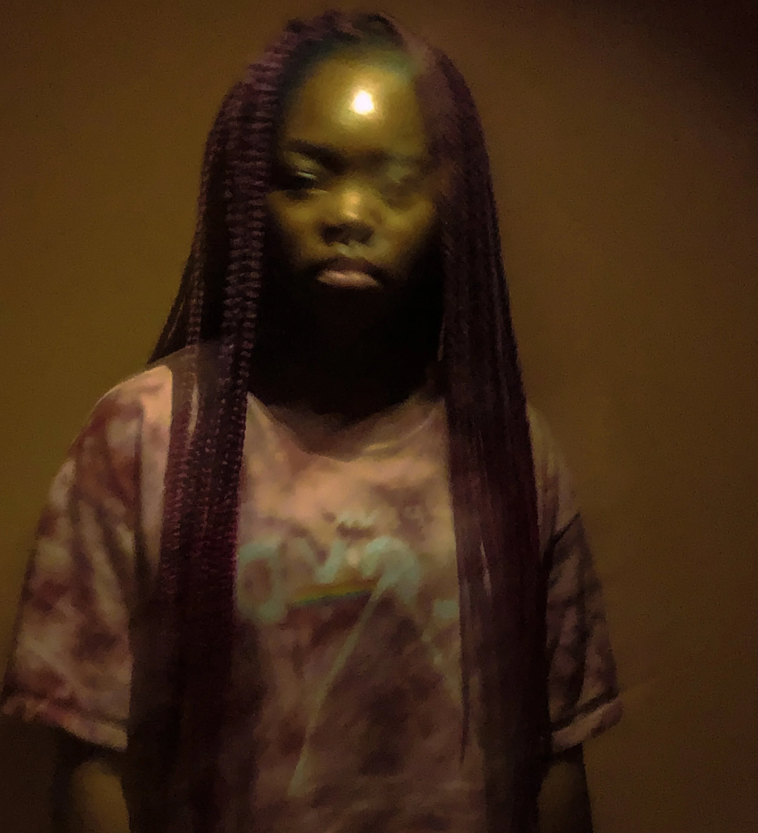 A woman with long burgundy box braids, wearing a Tie-dye shirt featuring a rainbow and clouds, standing against a plain, warm-colored background. Experimental photography. Shutter speed photography.