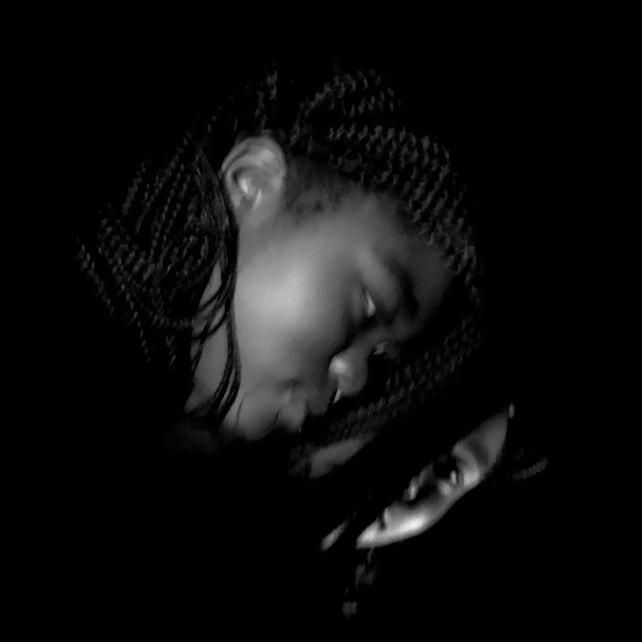 A black and white photo of a woman with braided hair sleeping with her hand near her face. Spotlight photography. Black and white spotlight photography. 