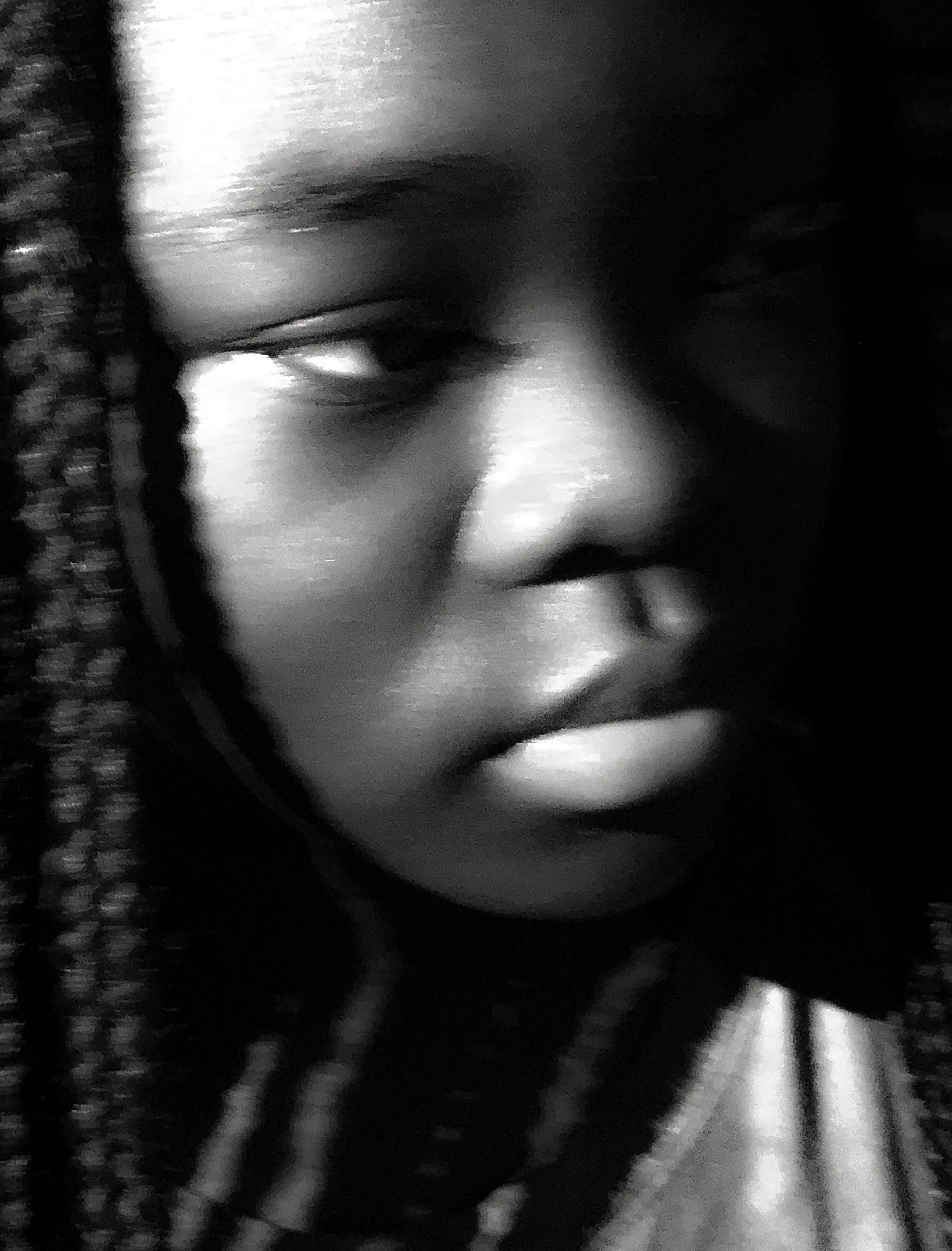 Close-up black and white photo of a woman's face with braided hair, showing her eye, nose, and lips.