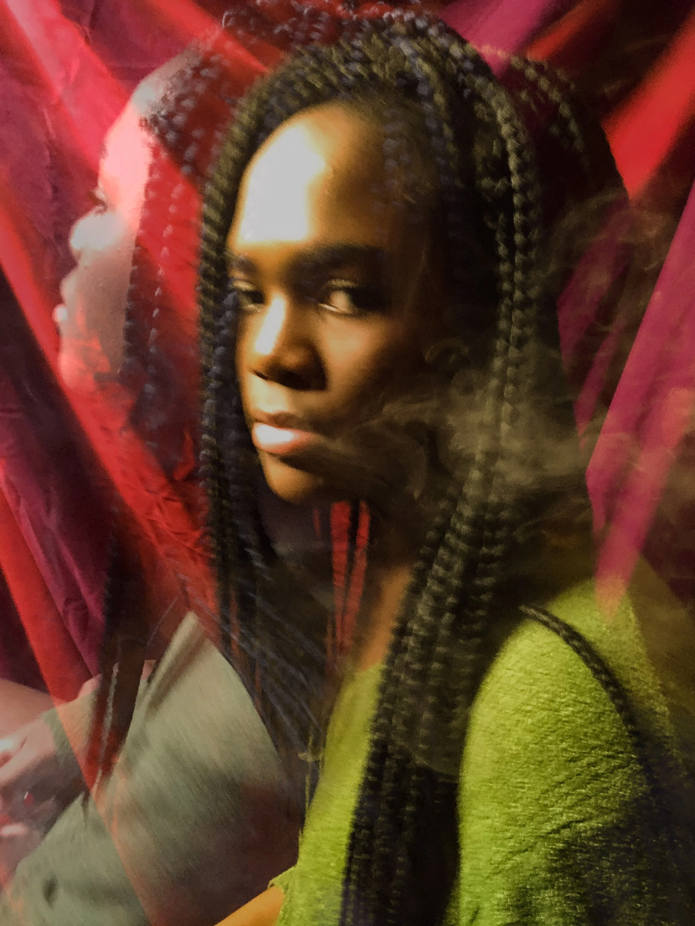 Portrait of a woman with braided hair, wearing a yellow top, behind a red and pink semi-transparent curtain or screen.