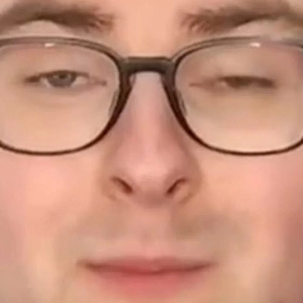 Close-up of a person's face with glasses, one eye partially closed and the other eye open.