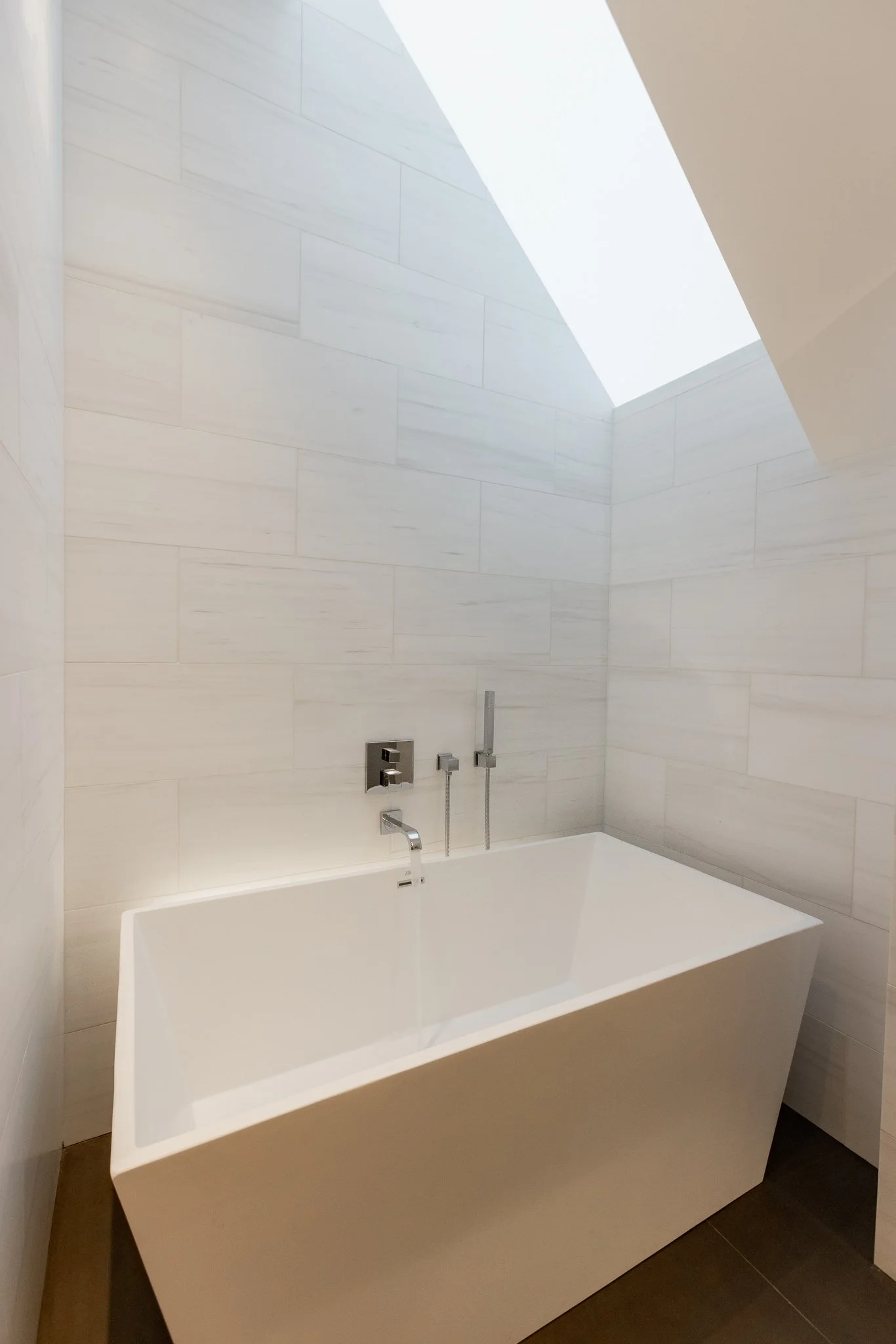 White rectangular bathtub in a modern bathroom with light-colored tiled walls and a skylight overhead.