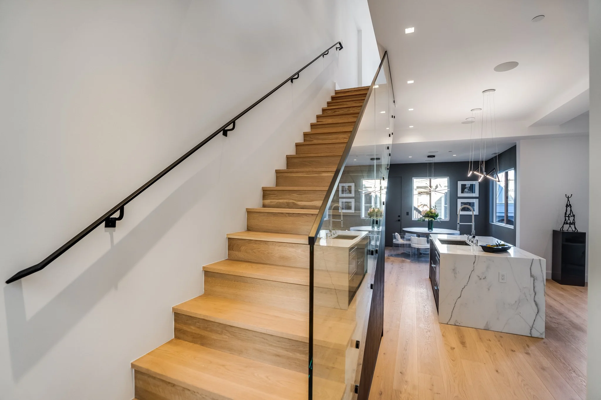 Modern interior with wooden staircase, open kitchen with marble island, pendant lighting, and large windows