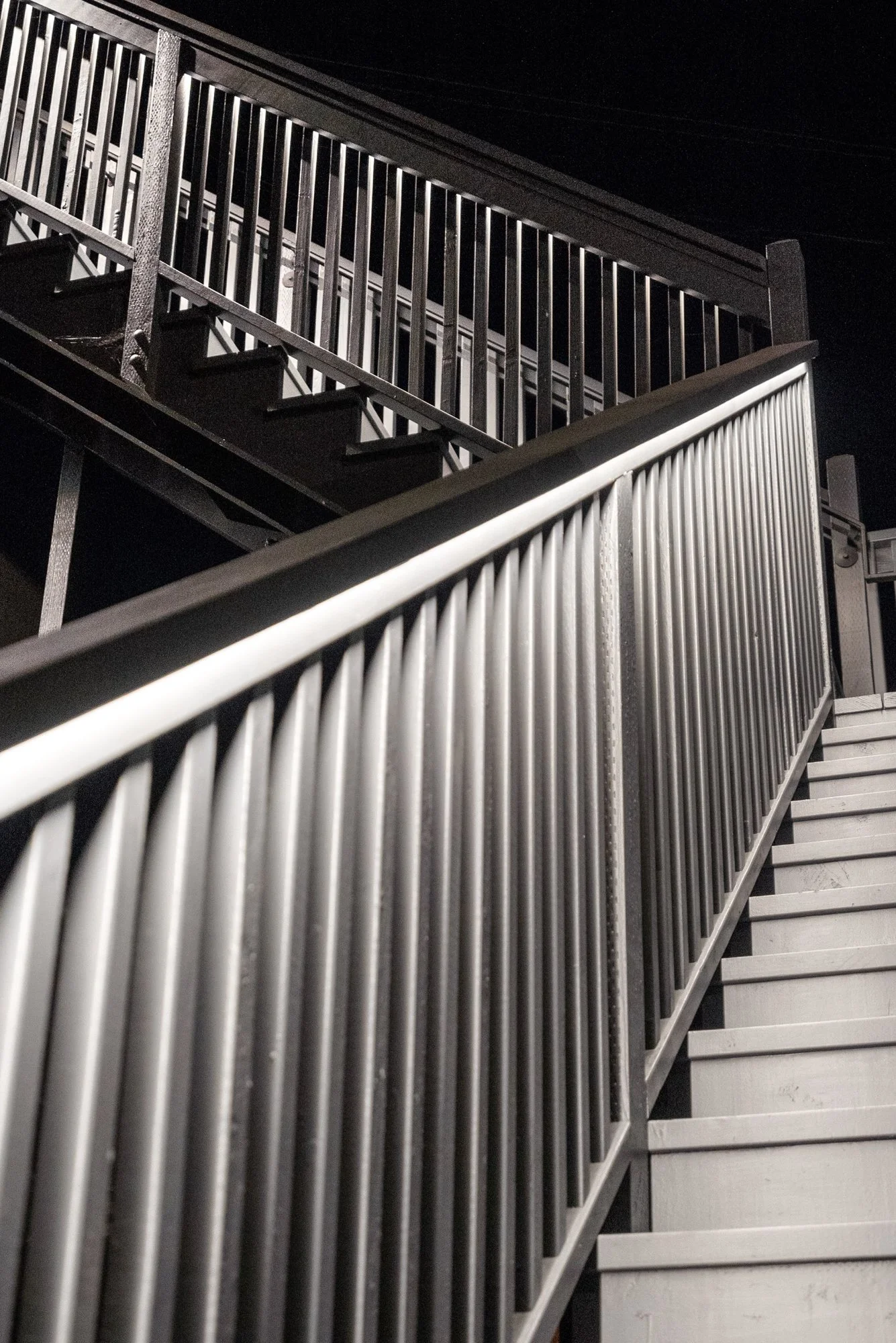 Nighttime view of metal staircase with railings, looking upward.