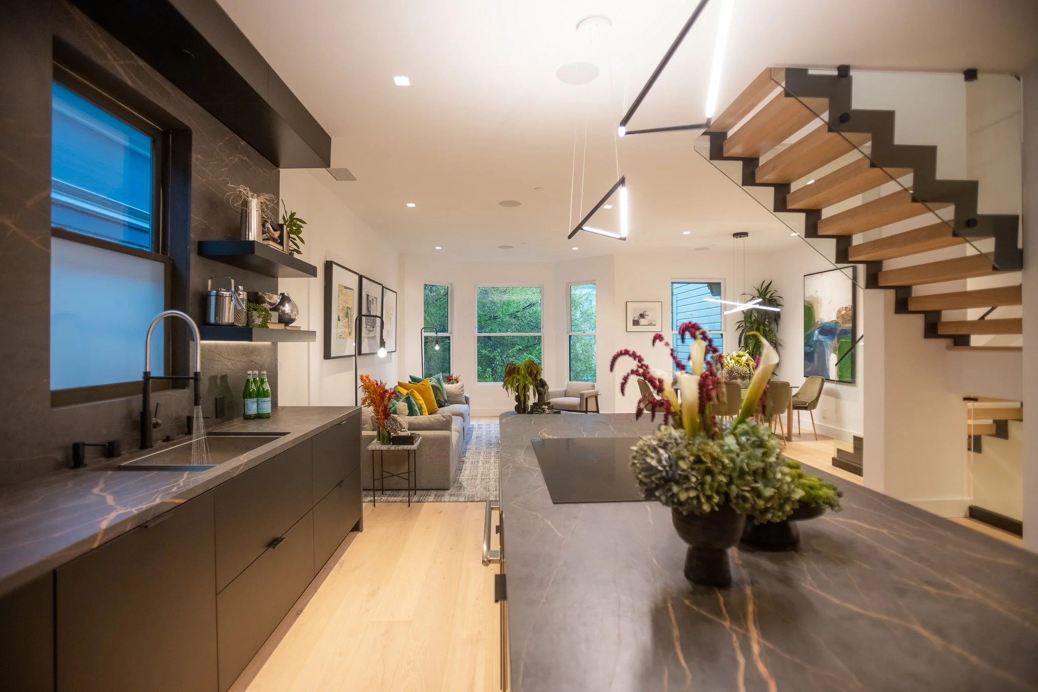 Modern open-concept living room and kitchen with large windows, colorful artwork, and contemporary furniture.