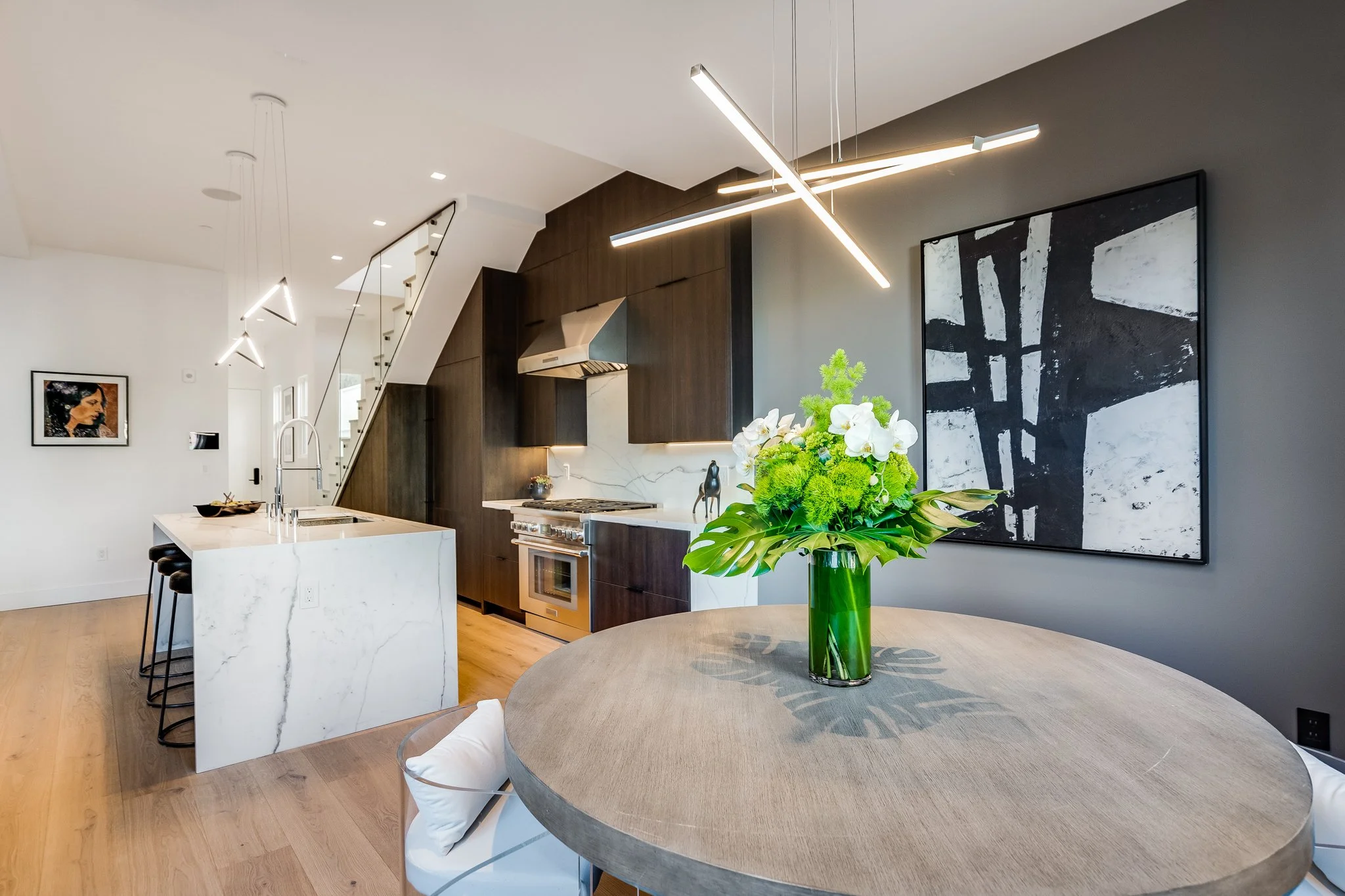 Modern kitchen and dining area with a round table, floral arrangement, dark gray and white walls, and contemporary lighting fixtures.