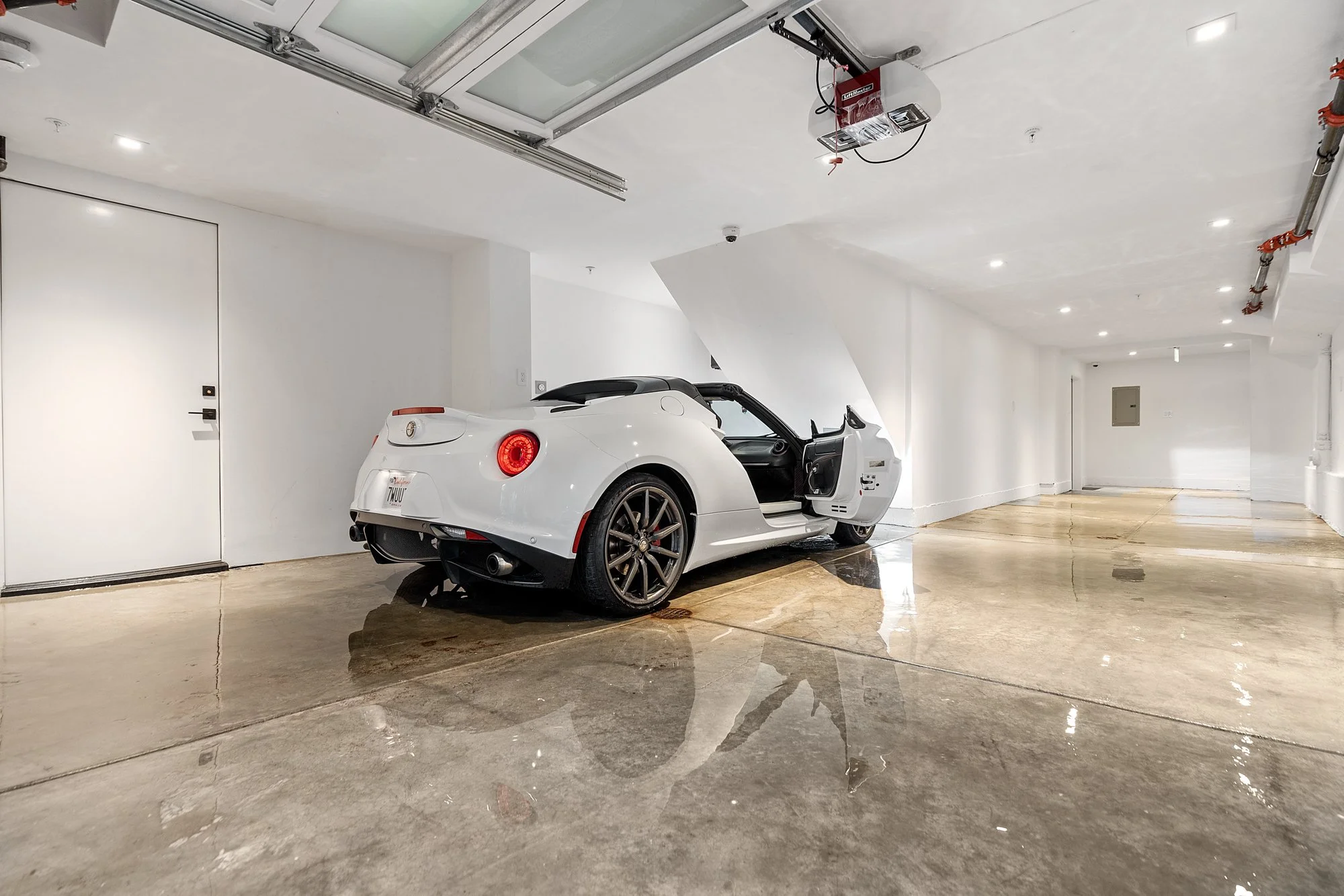 A white convertible sports car parked inside a clean, empty garage with white walls and a polished concrete floor.
