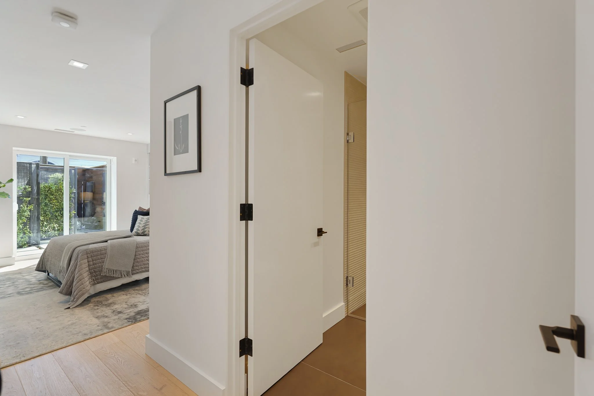 Open door leading to a bathroom or small closet, view into a bedroom with a bed, window, and sliding glass door.