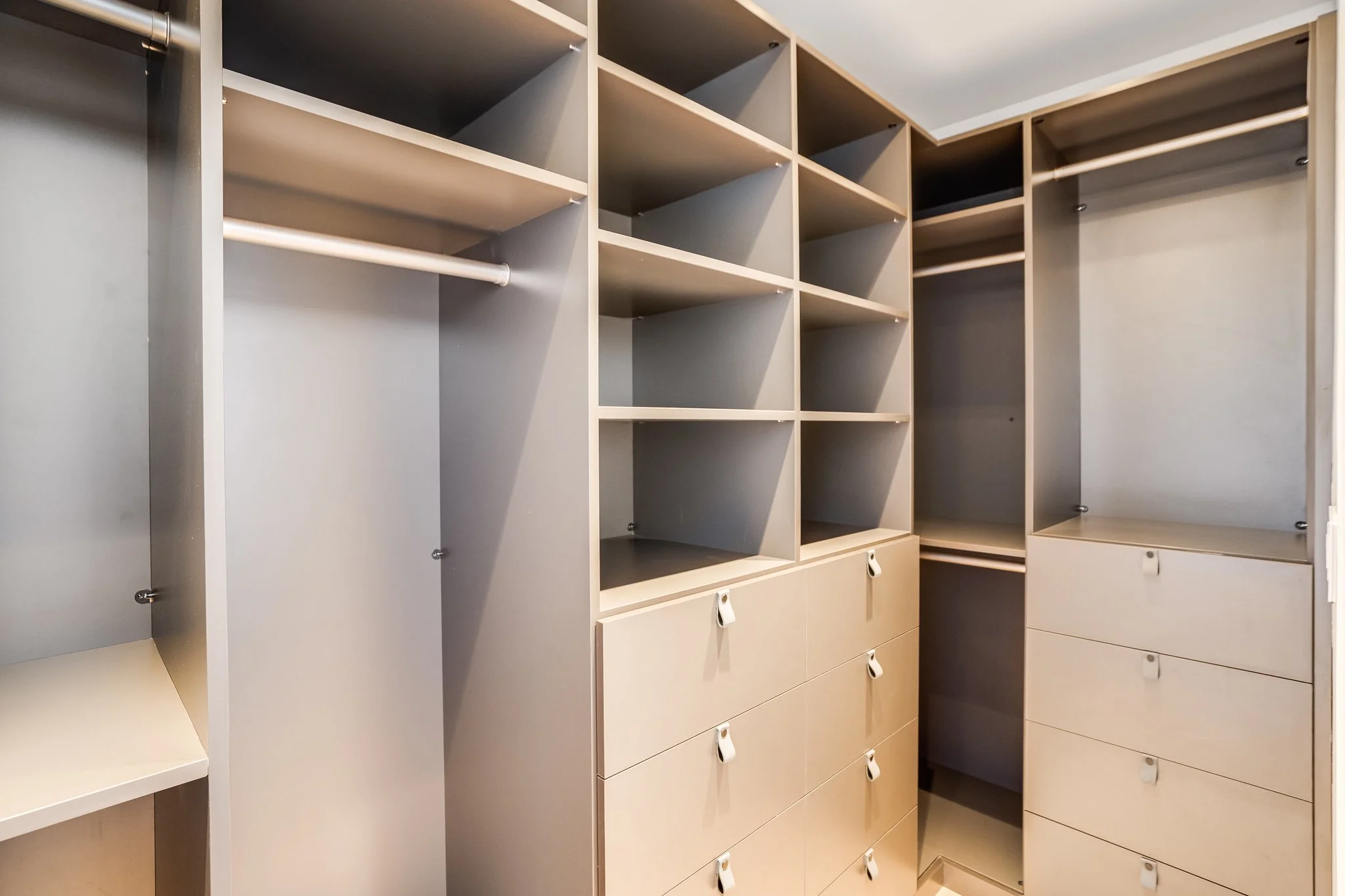Empty wooden closet with multiple compartments, shelves, and drawers, some with hanging rods.