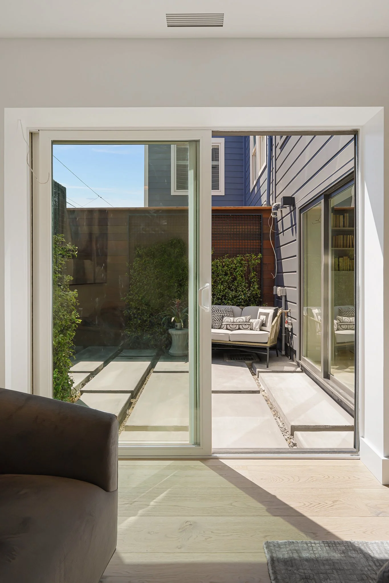 Sliding glass door opening to a small outdoor patio with modern seating, greenery, and a wooden privacy fence.