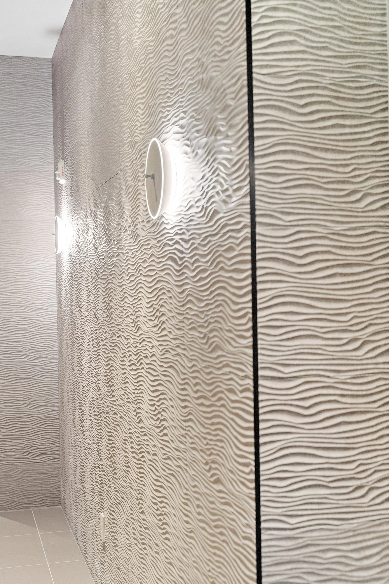 Close-up of a textured beige wall with wavy patterns, two white circular ceiling lights, and a black vertical line on the right side.