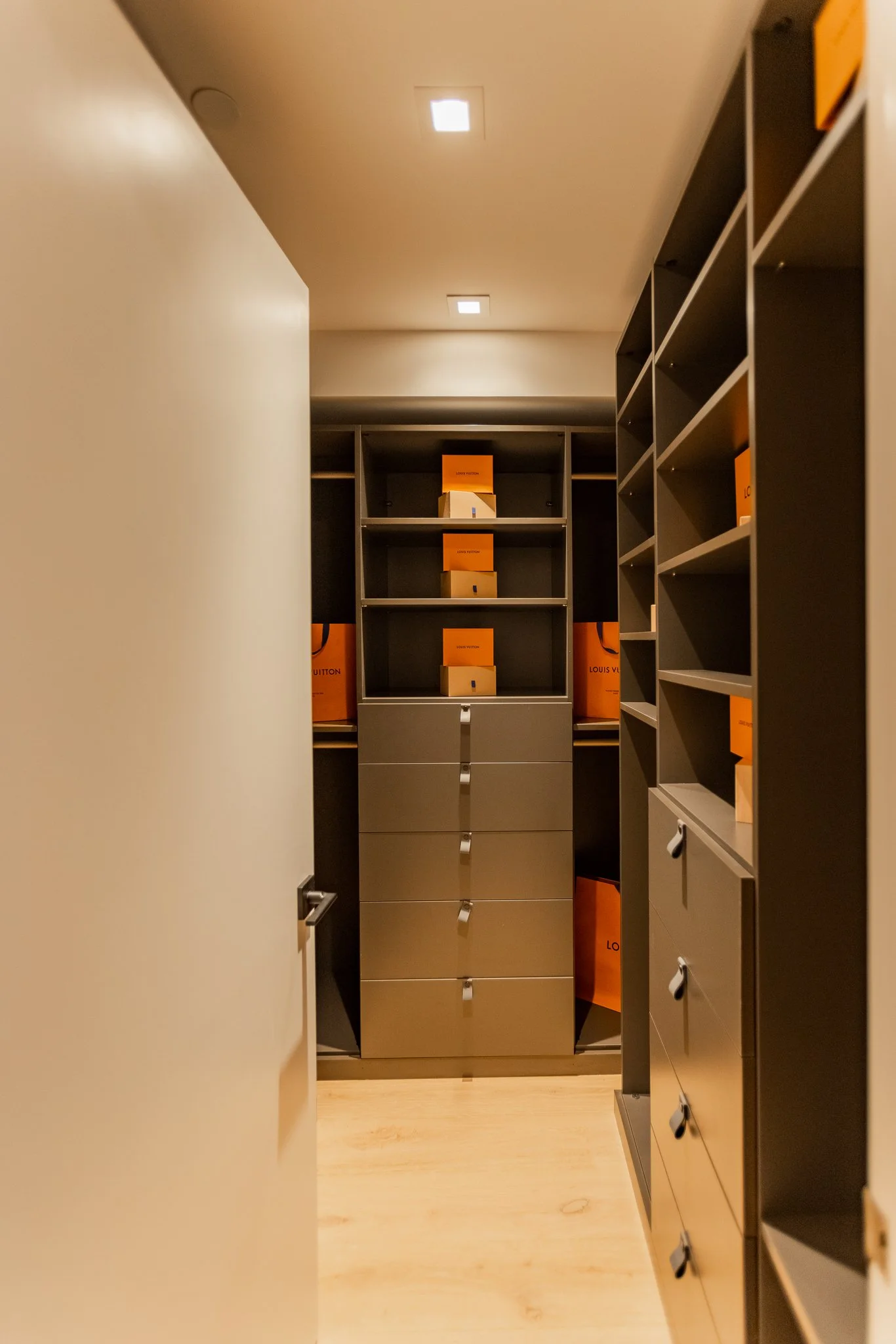 A walk-in closet with gray shelves and drawers, some containing orange Louis Vuitton boxes, viewed from the doorway.