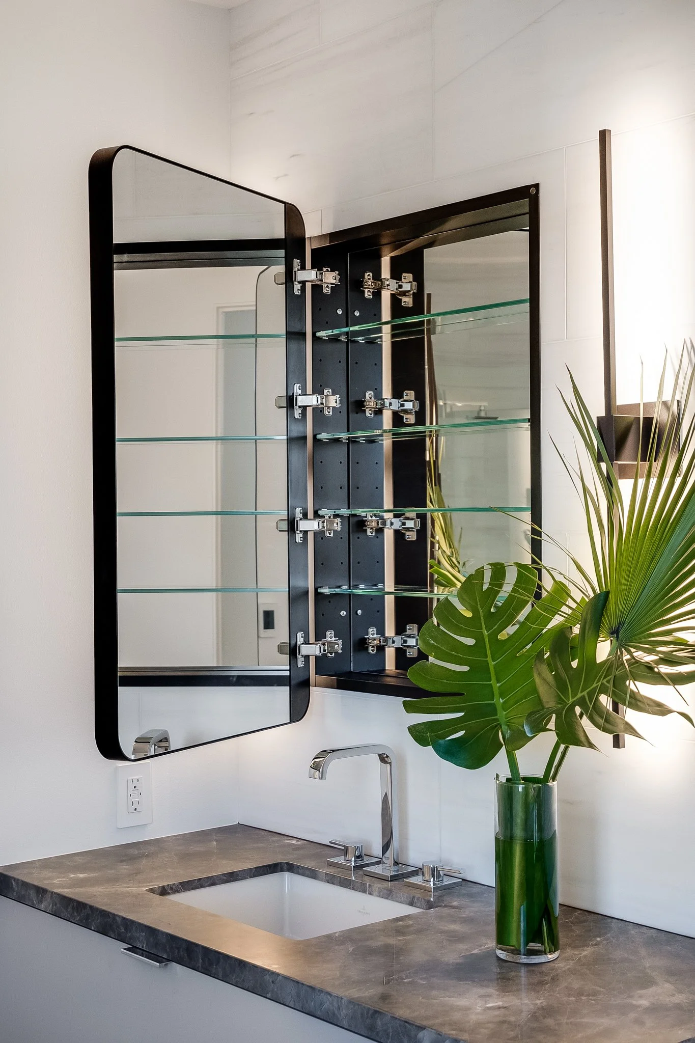 Modern bathroom with a mirror, a vessel sink, a faucet, and a large plant in a green vase.