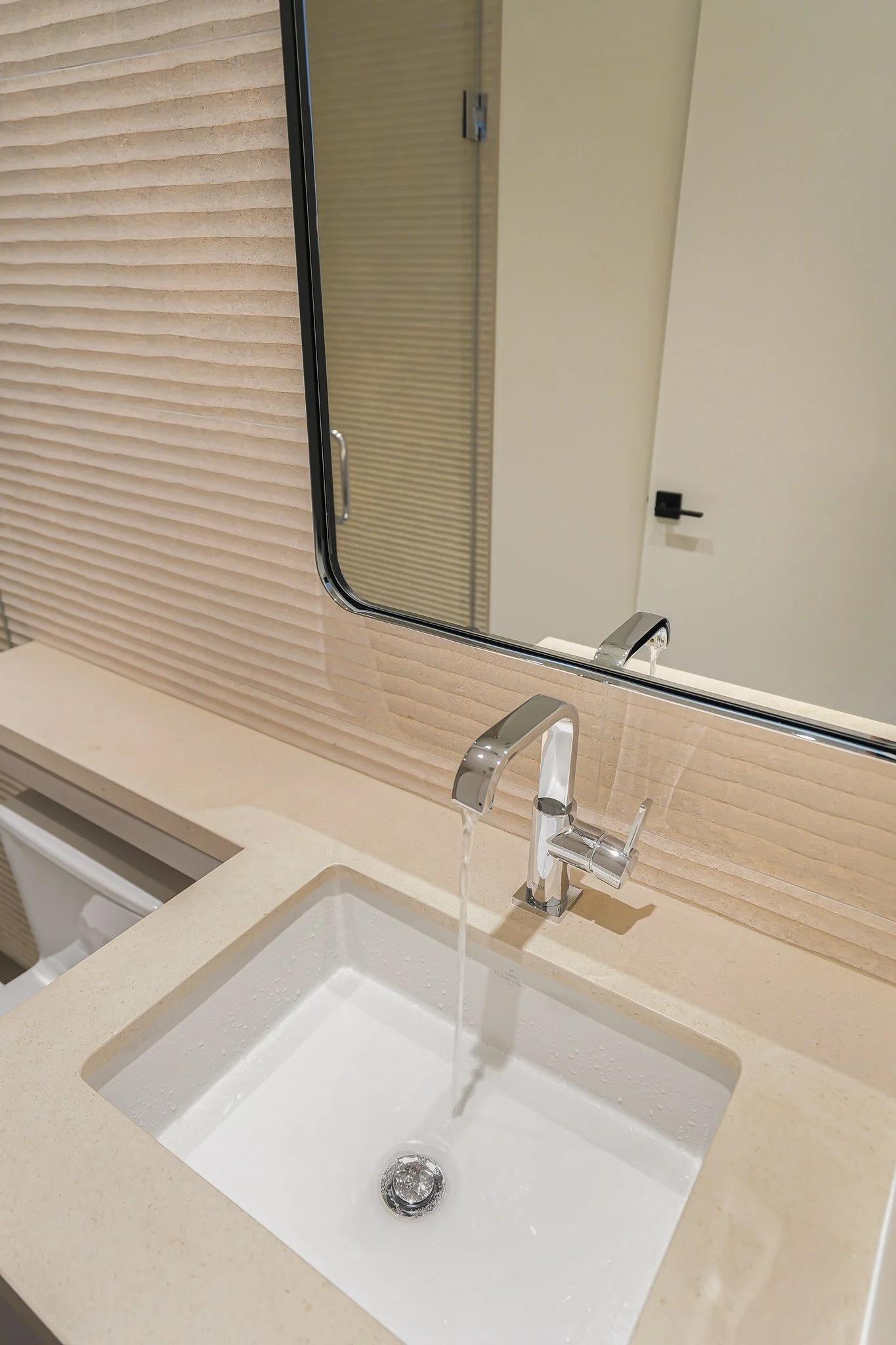 A bathroom sink with a mirror above it, a running faucet, and a beige countertop.