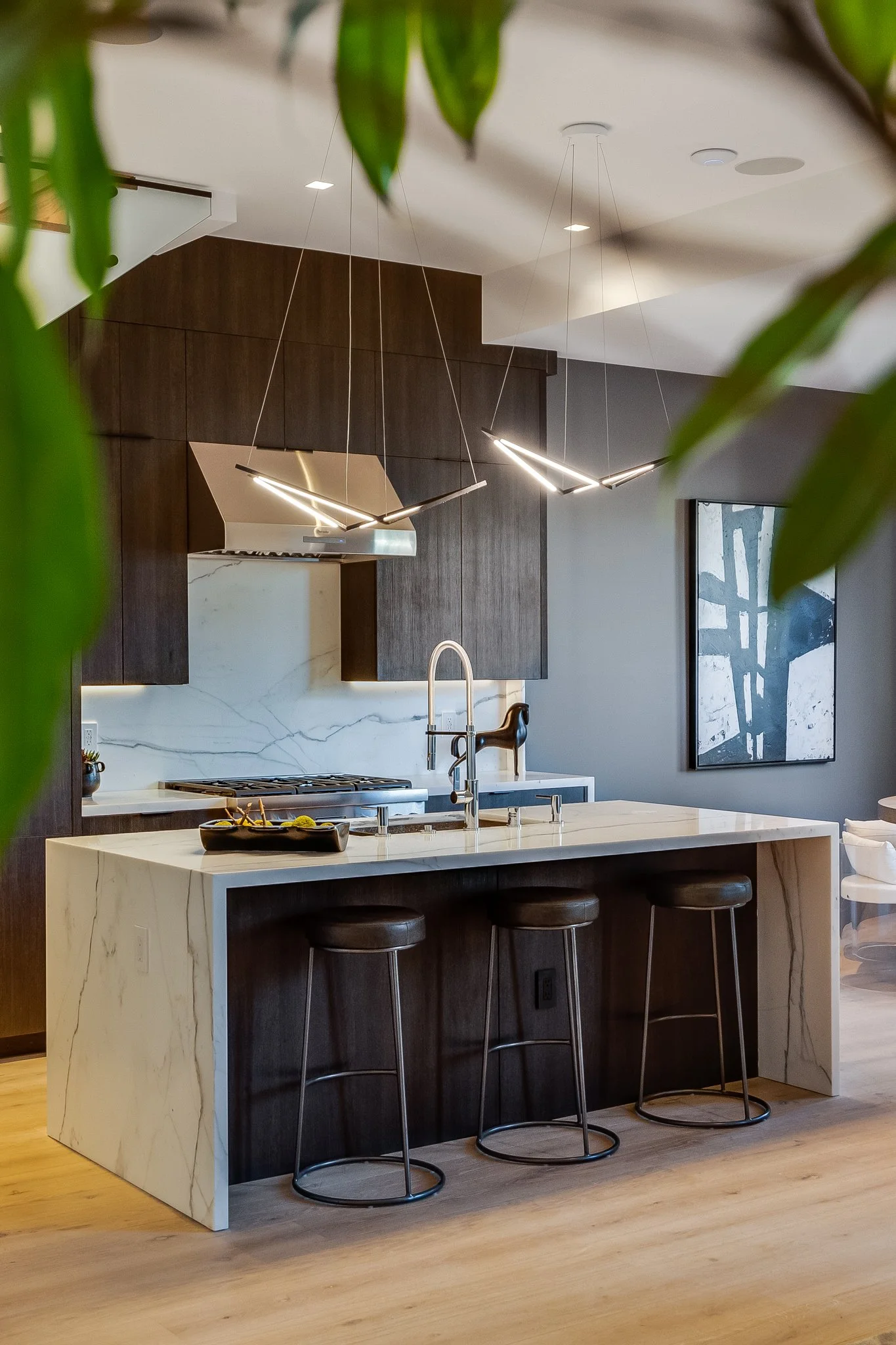 Modern kitchen with dark wood cabinets, marble island, and artistic lighting fixtures