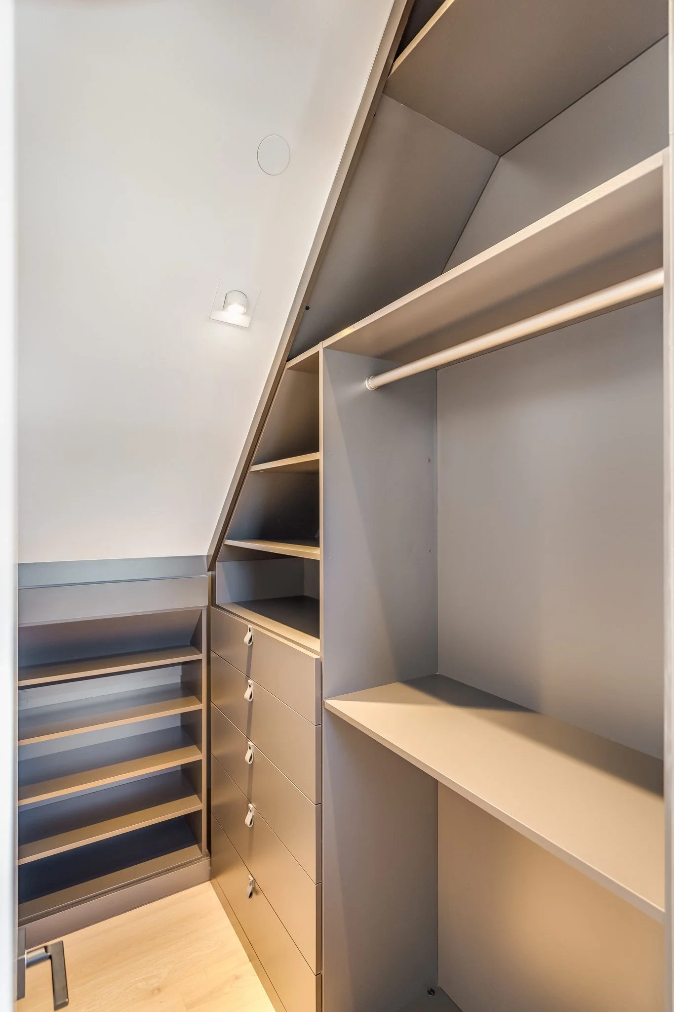 Empty walk-in closet with shelves, drawers, and hanging space under a sloped ceiling.