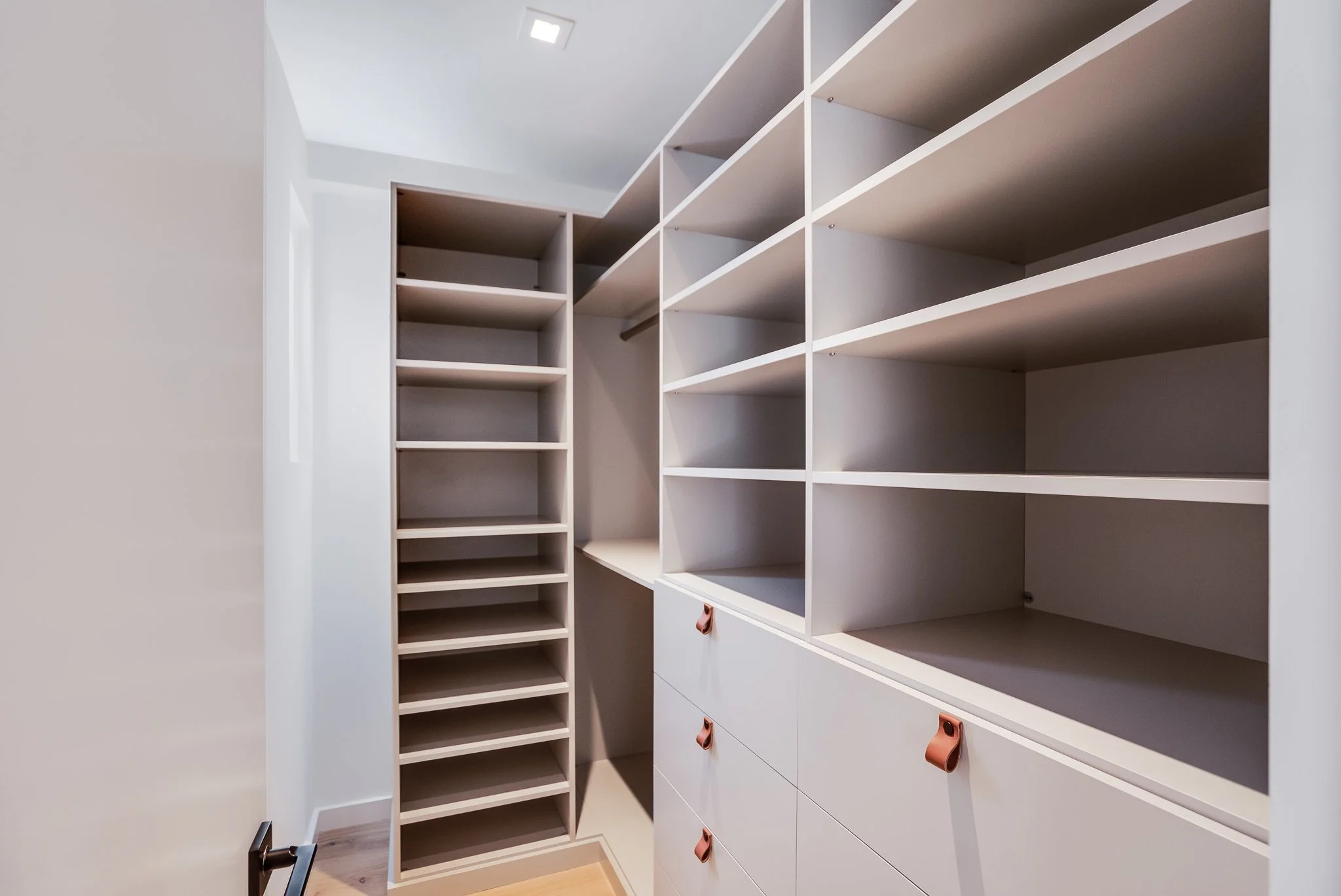 Empty walk-in closet with white shelves, drawers, and a hanging rod.