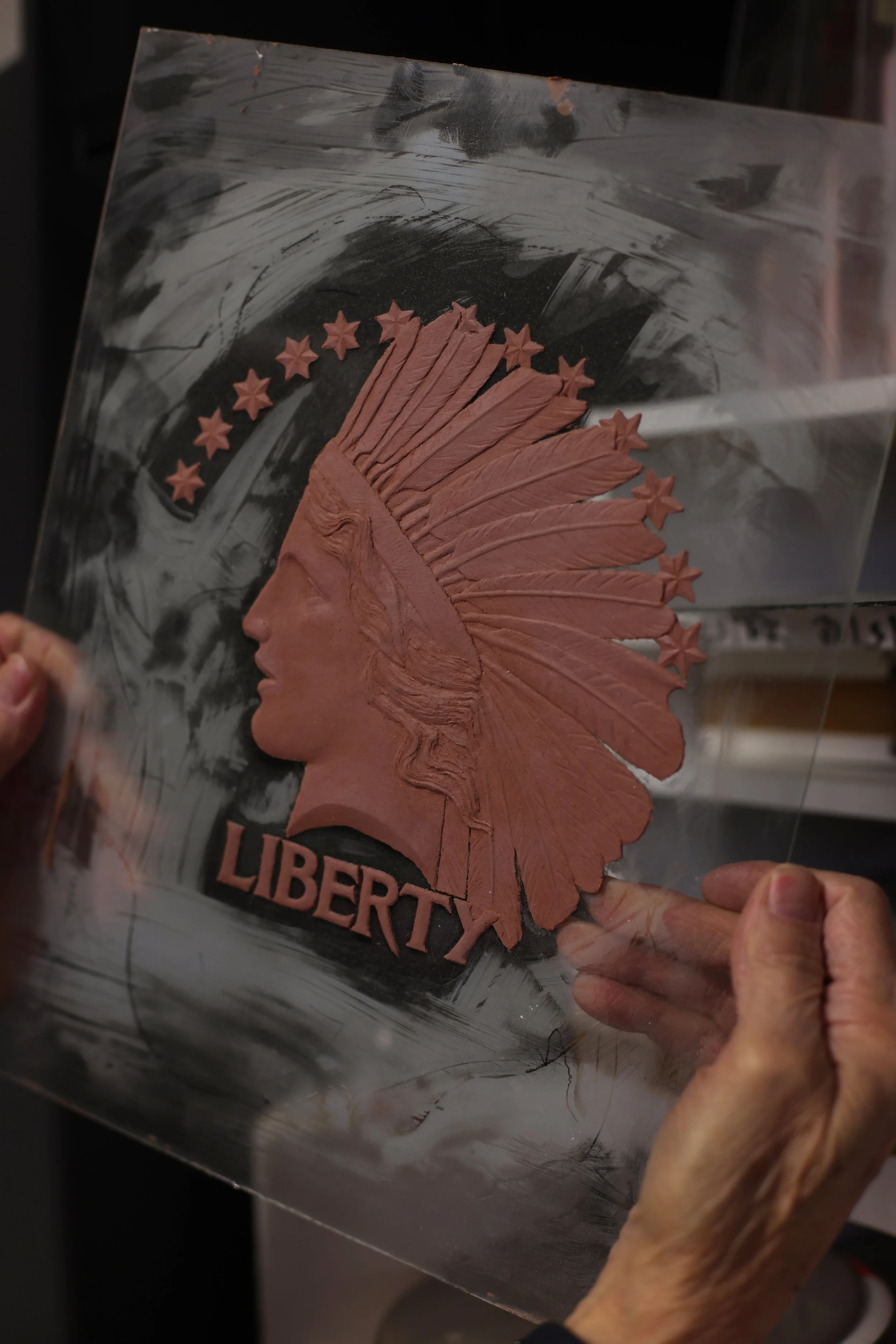 Clay relief model of a Liberty portrait with a Native American headdress, illustrating the sculptural design process used in creating coins and medals.