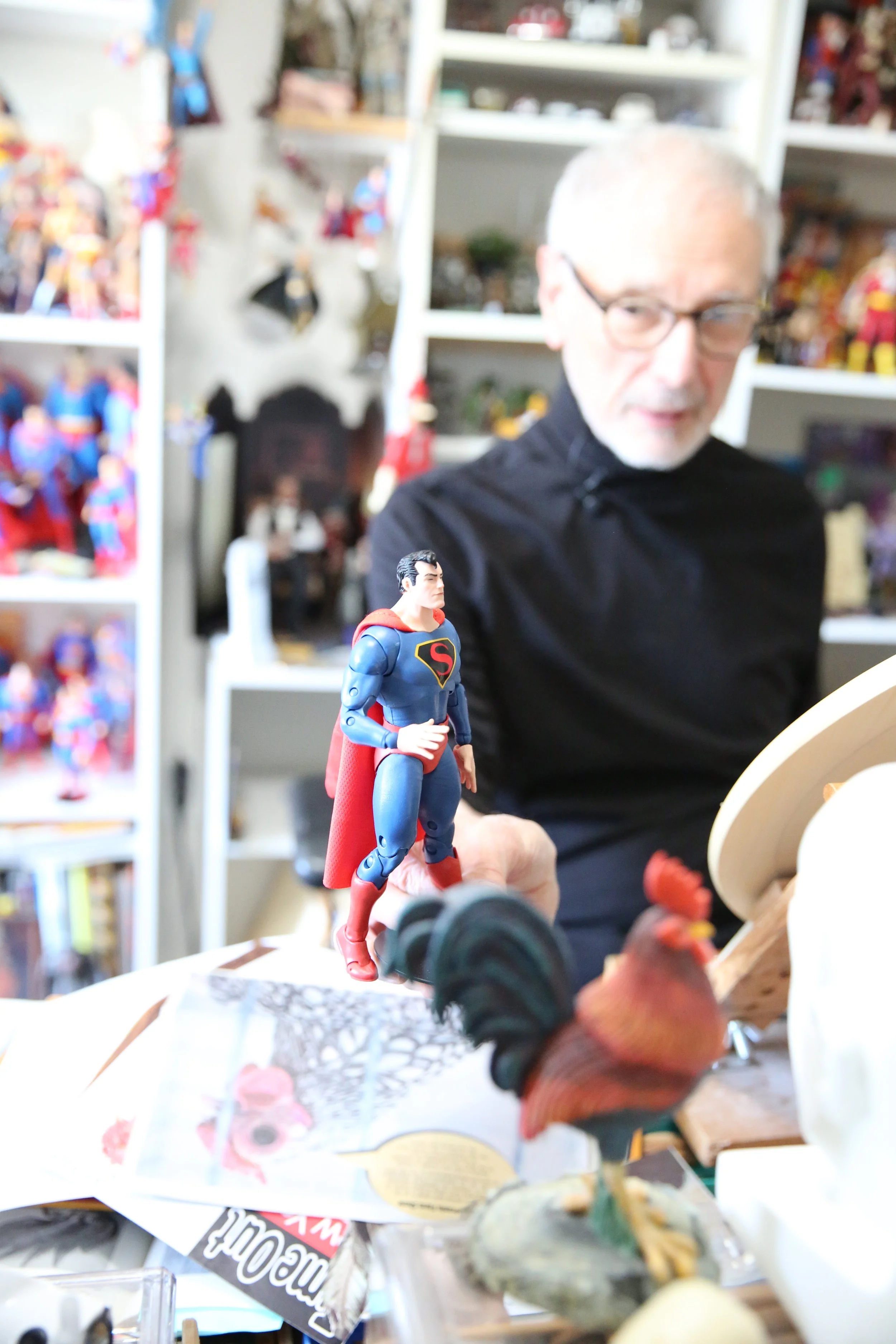 John Mercanti working in his home studio, surrounded by personal collectibles and creative projects, offering a glimpse into the artistic environment behind his coin and medal designs.