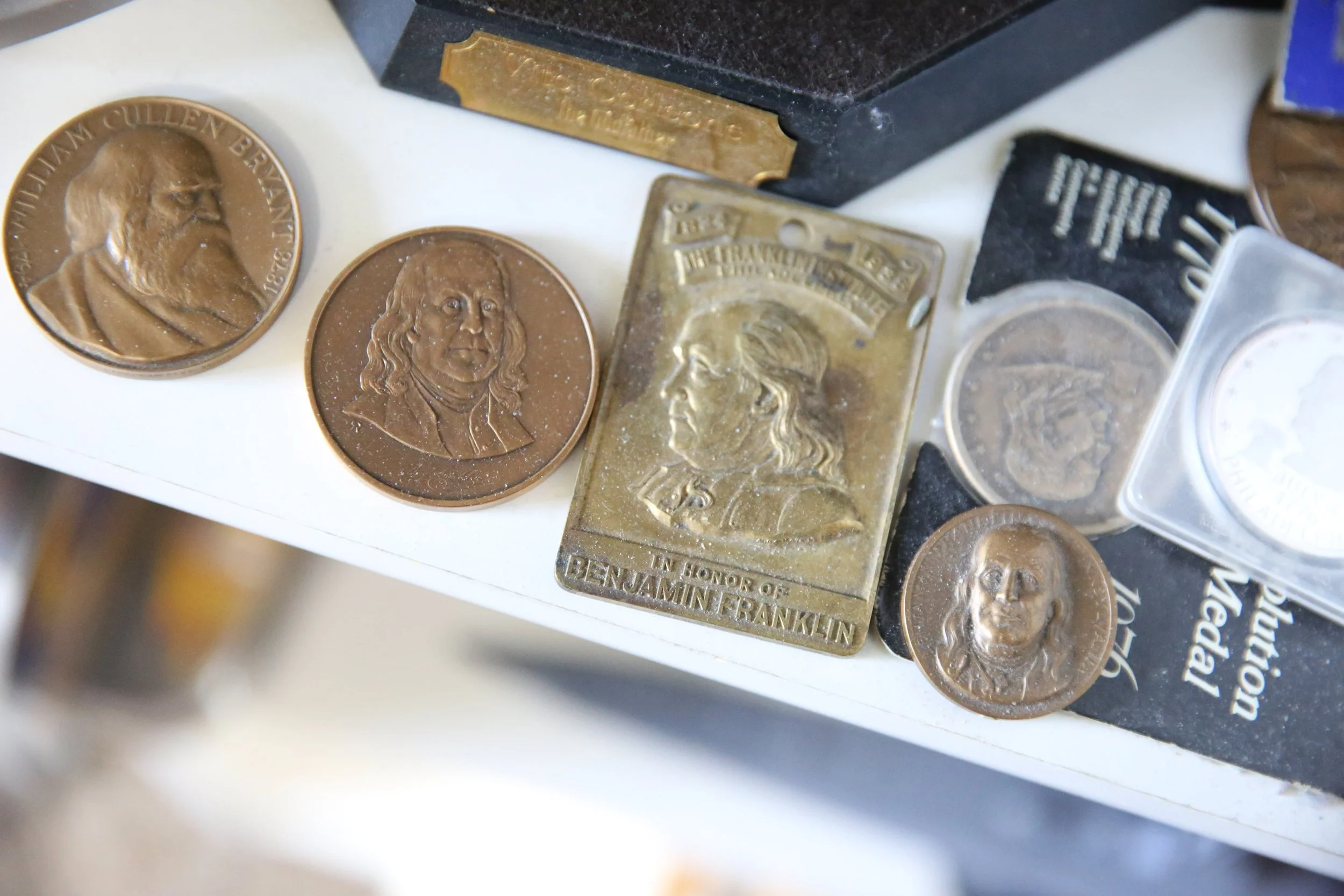Benjamin Franklin coin and medal design prototypes displayed in an artist's studio, showcasing the development of numismatic artwork and collectible coin concepts.