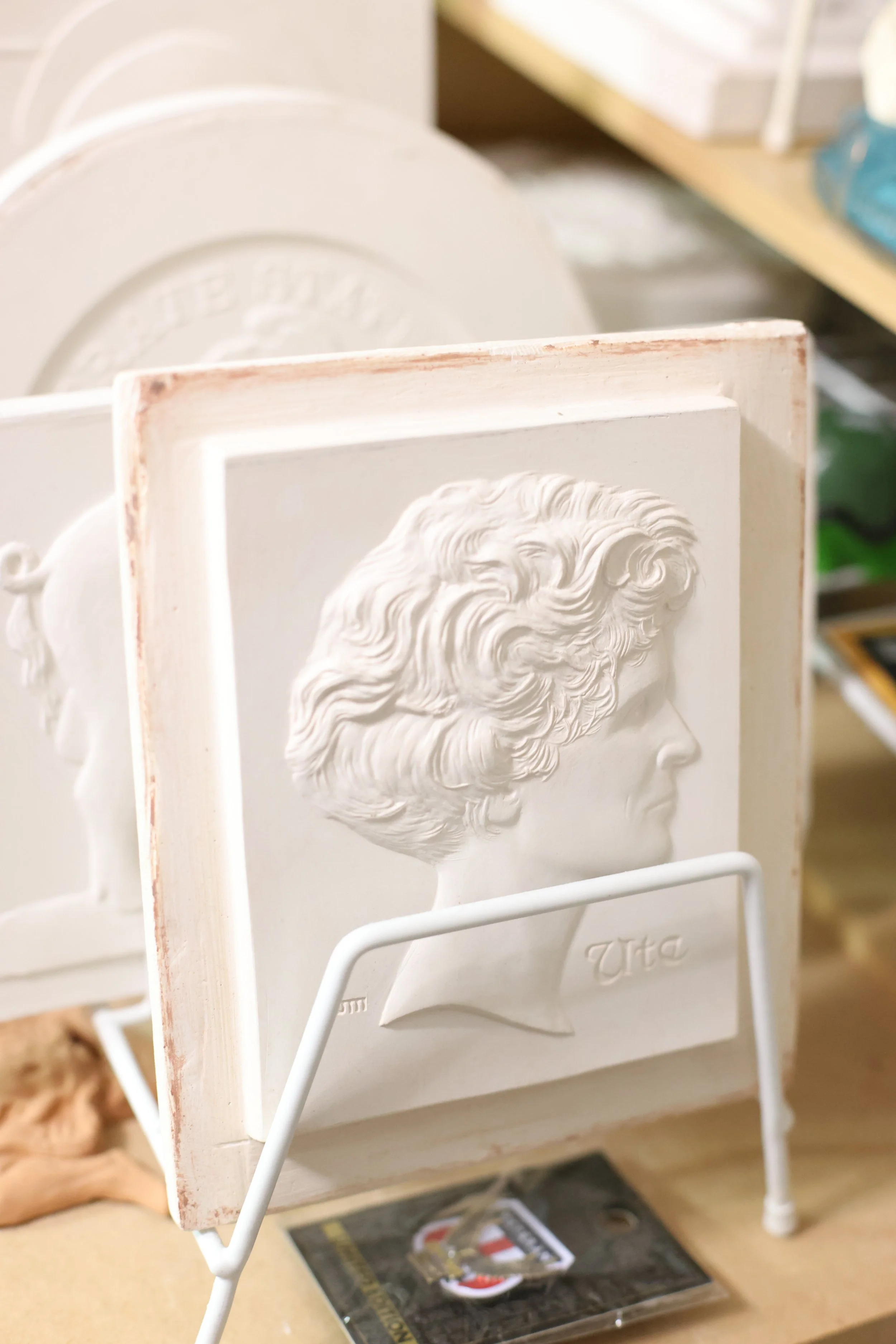 Plaster relief portrait model used in coin and medal design, showcasing the sculptural craftsmanship involved in transforming artistic concepts into finished collectible pieces.