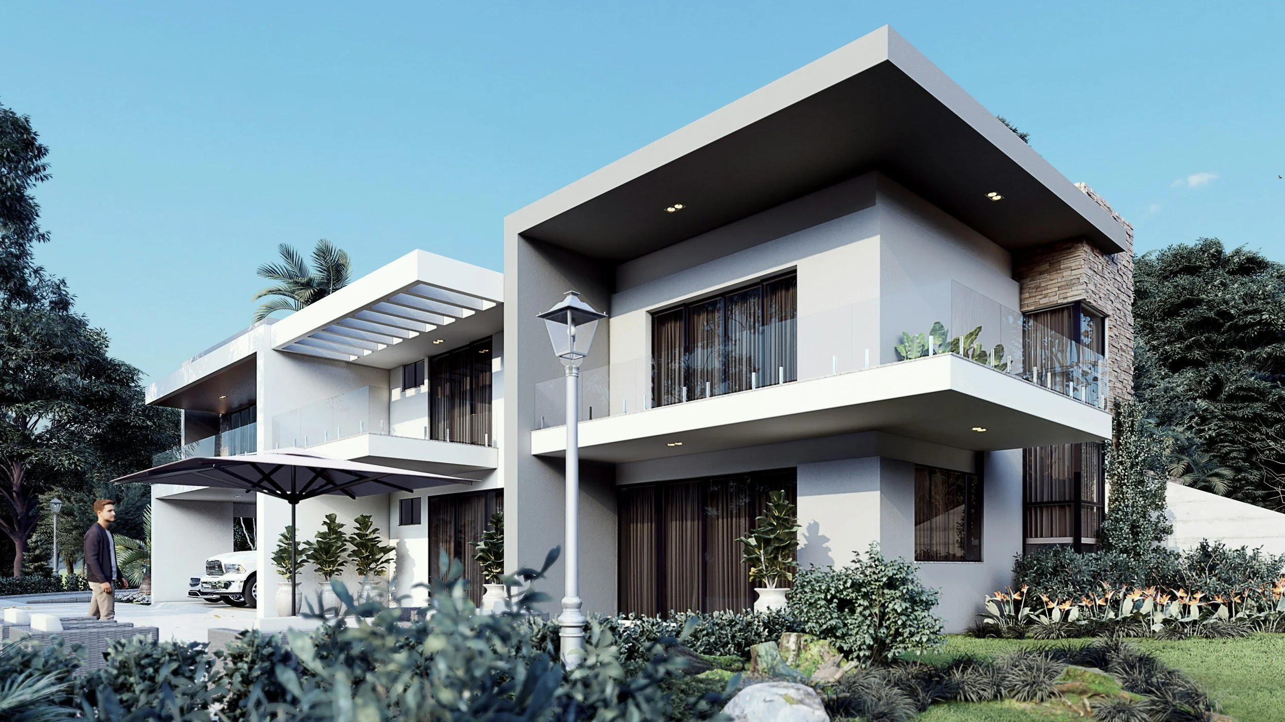 Modern two-story house with large balconies, glass railings, and an outdoor seating area with a large umbrella. There are landscaped gardens, plants, and a man walking near the house, with trees and a blue sky in the background.