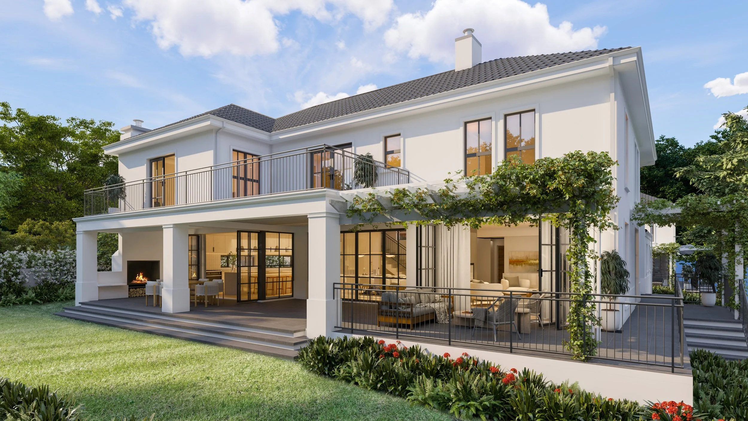 Exterior view of a modern white two-story house with large glass doors and windows, a balcony with black railing, outdoor fireplace with chairs, and lush garden with green grass and flowering plants under a partly cloudy sky.