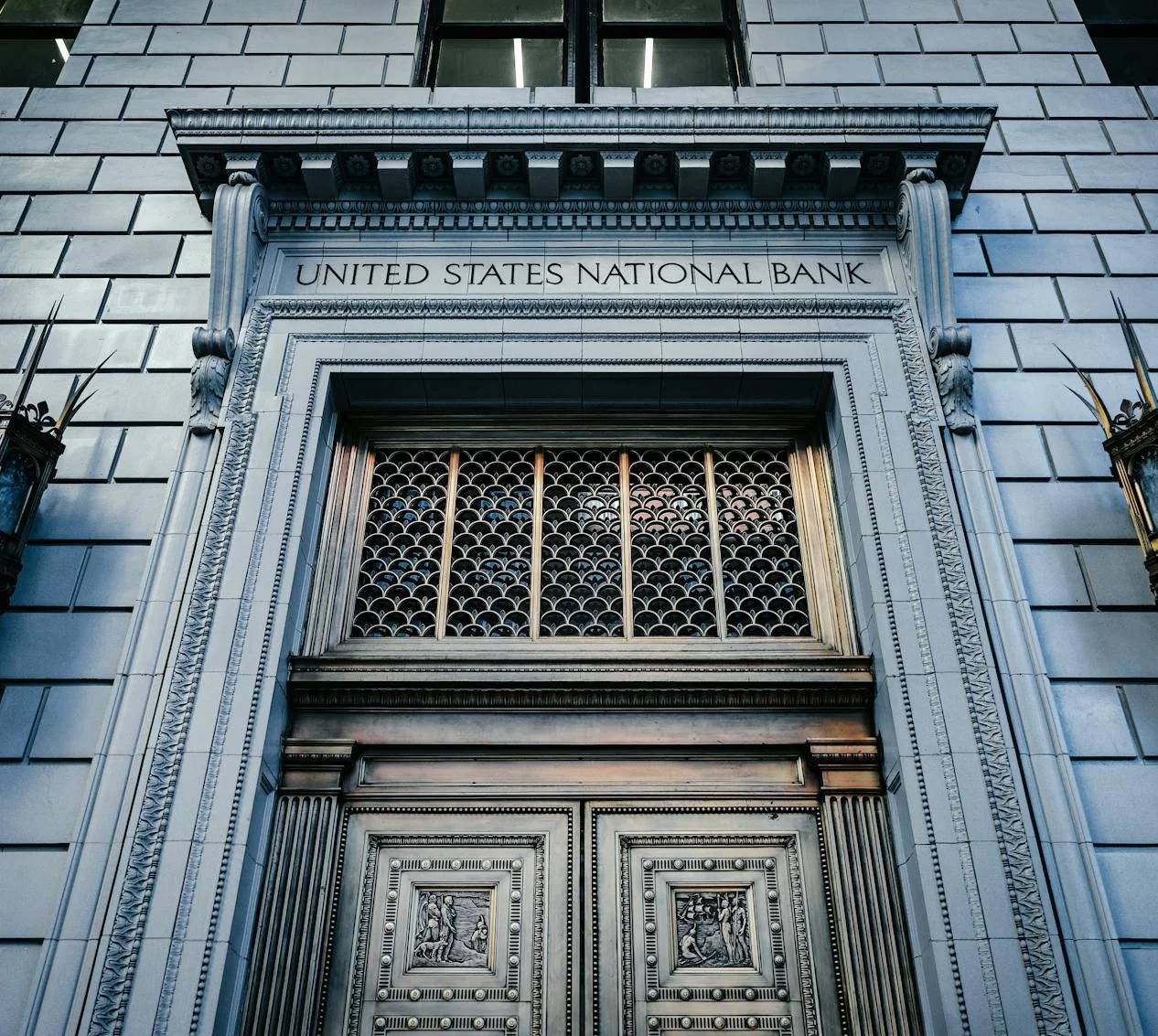 Front entrance of a historic building labeled 'United States National Bank' with ornate carved details, metal gates, and decorative elements.