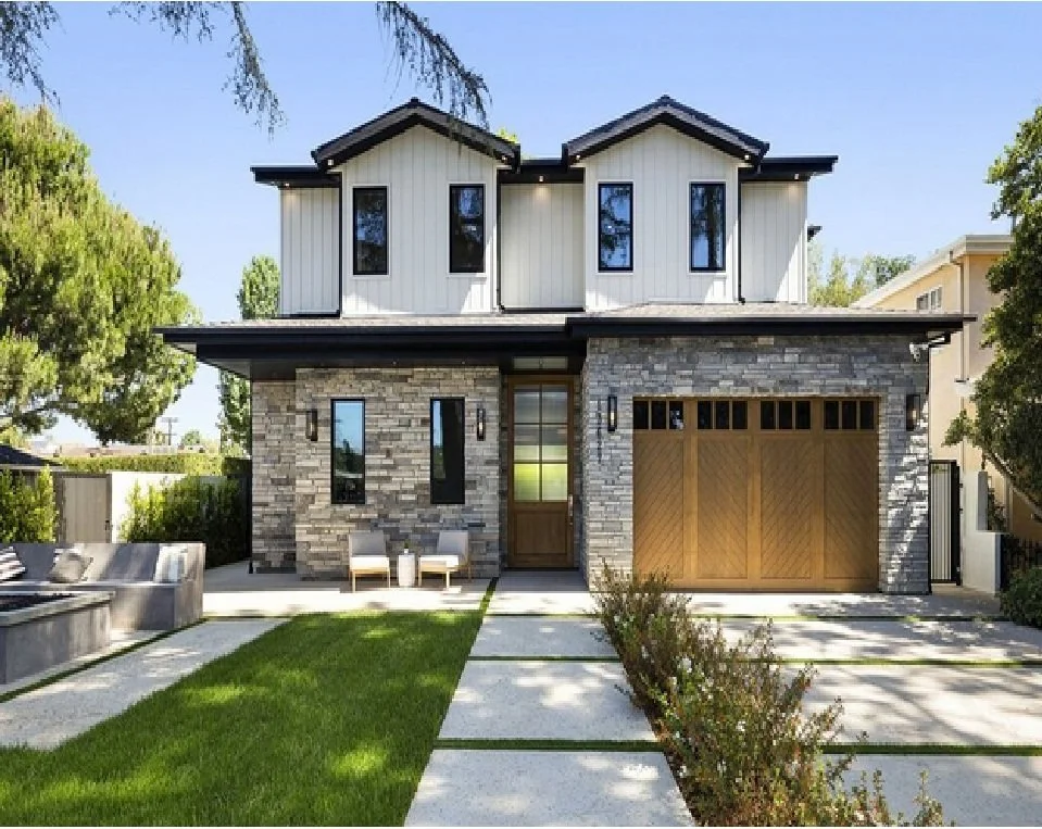 Front view of a modern two-story house with stone and white siding, a wooden garage door, and a small lawn with a walkway.