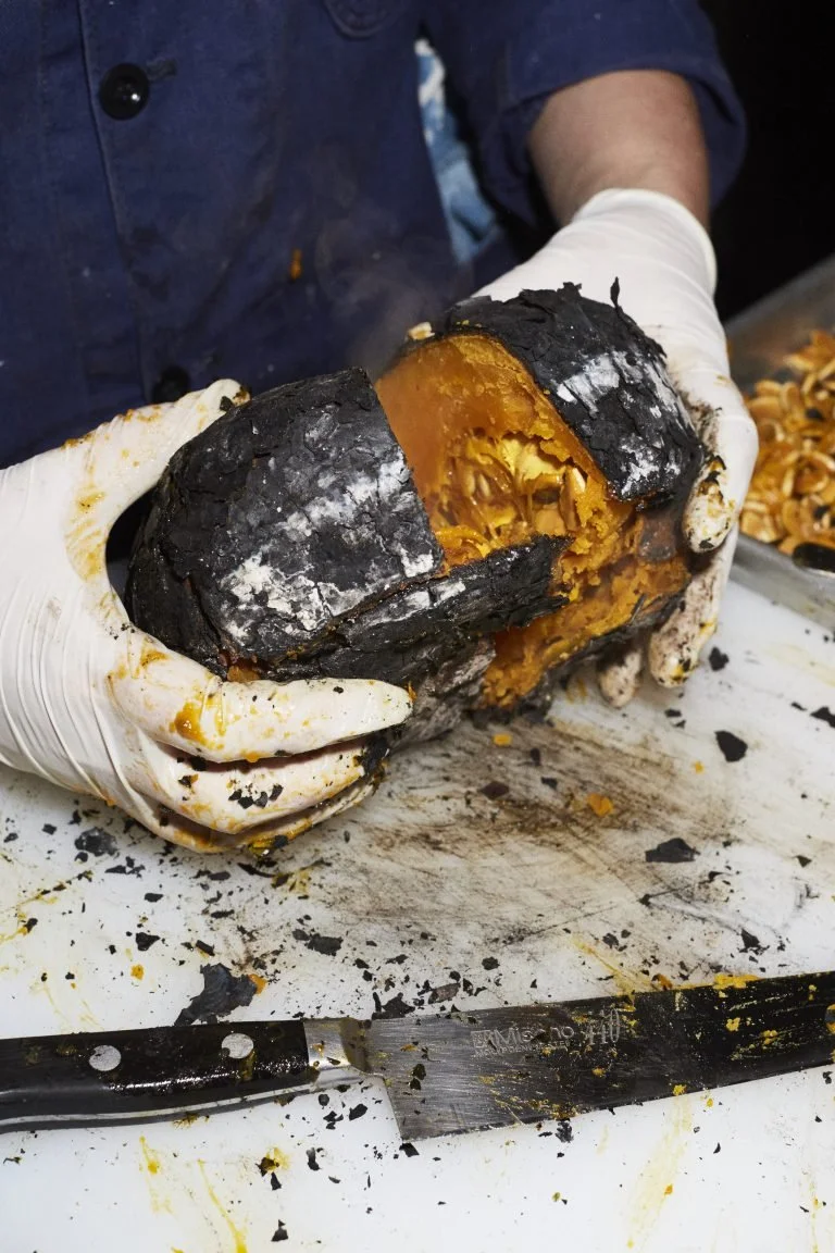 Person wearing white gloves holding a large, charred, blackened pumpkin, showing its bright orange interior.