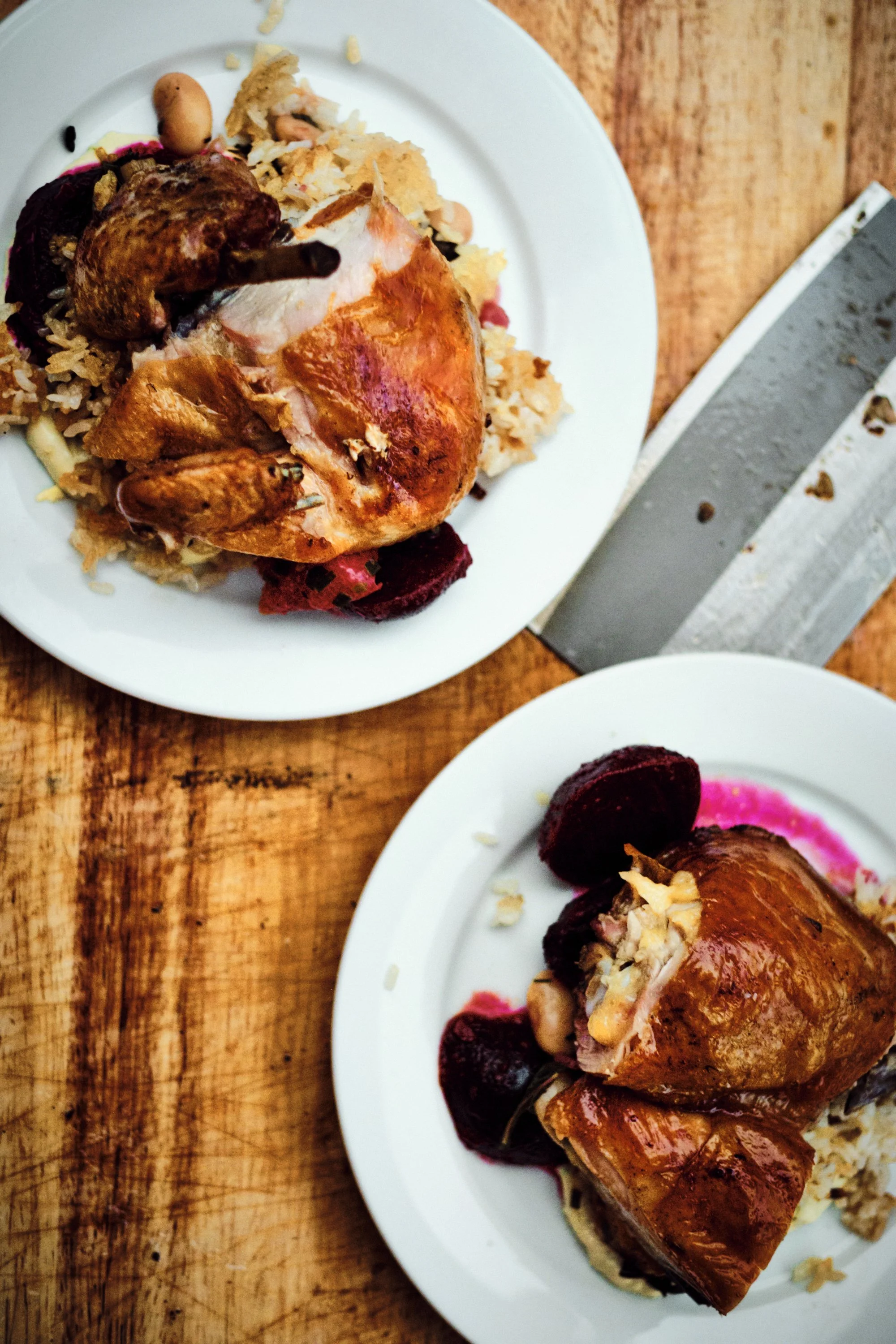 Roast chicken served on white plates with rice and beets on a wooden table.