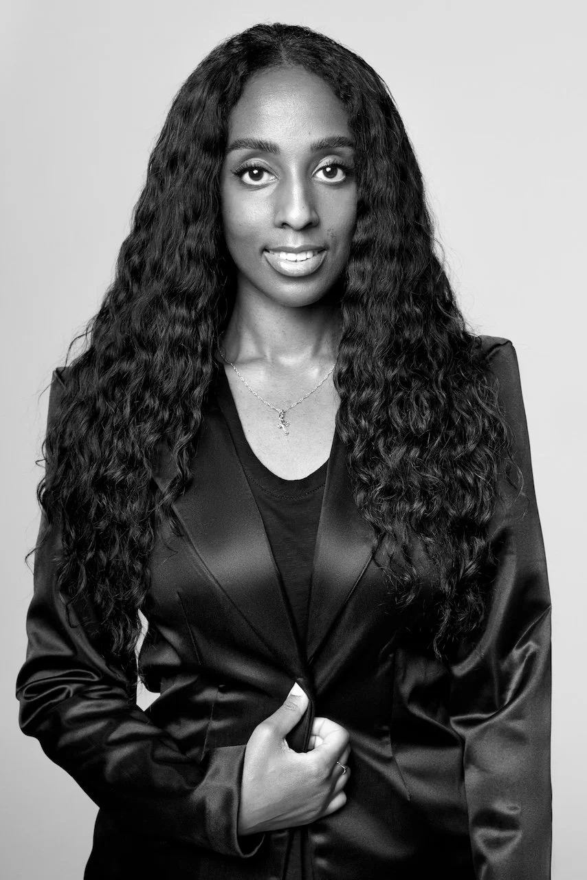 Black and white portrait of a woman with long wavy hair, wearing a blazer and a necklace
