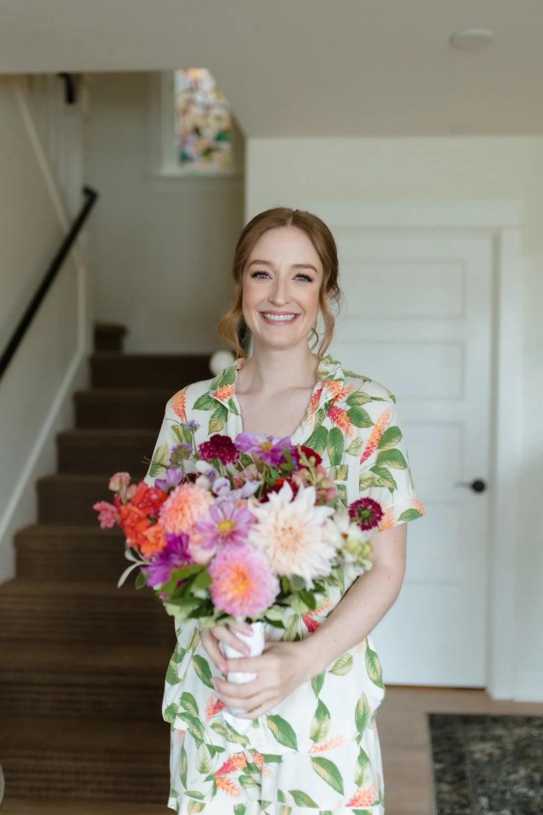 A woman with red hair in floral pajamas holding a colorful bouquet of flowers in a home interior