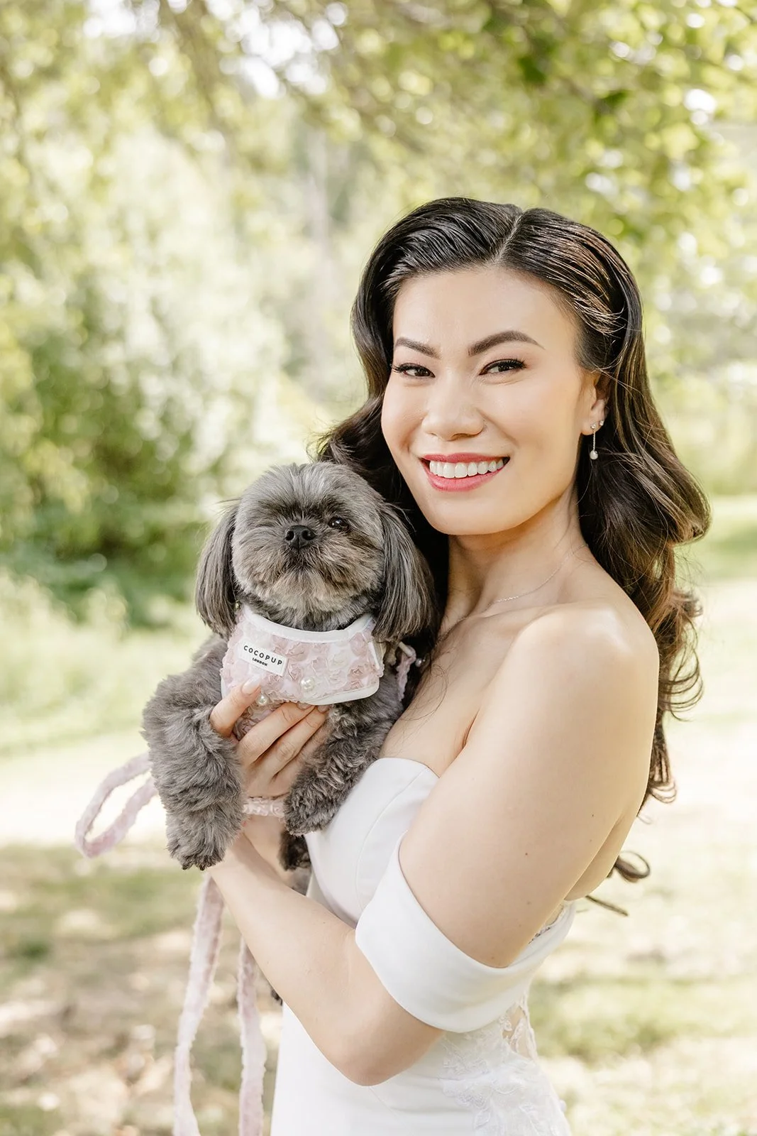 A woman with dark, wavy hair wearing a strapless white dress, smiling while holding a small gray dog in an outdoor park setting with green trees in the background.
Makeup and hair Stace Cho
Photographer Taylor Ochoa, Tminspired
Venue Jardín del sol