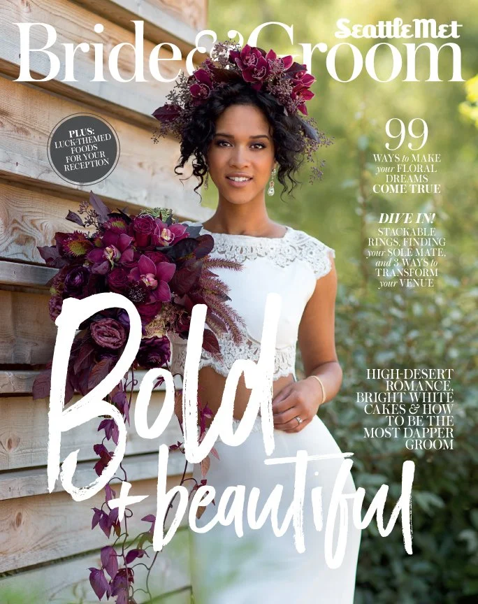 Magazine cover featuring a woman in a white lace dress holding a large bouquet of dark purple flowers, standing outdoors against a wooden wall with greenery in the background. Headline reads 'Bold & Beautiful' with other smaller headlines about weddi
