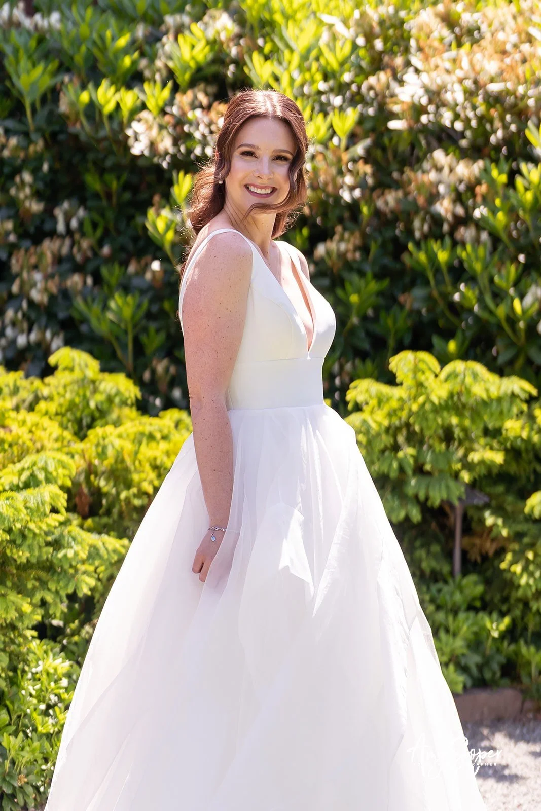 A young woman in a white dress smiling outdoors with green and yellow foliage in the background.