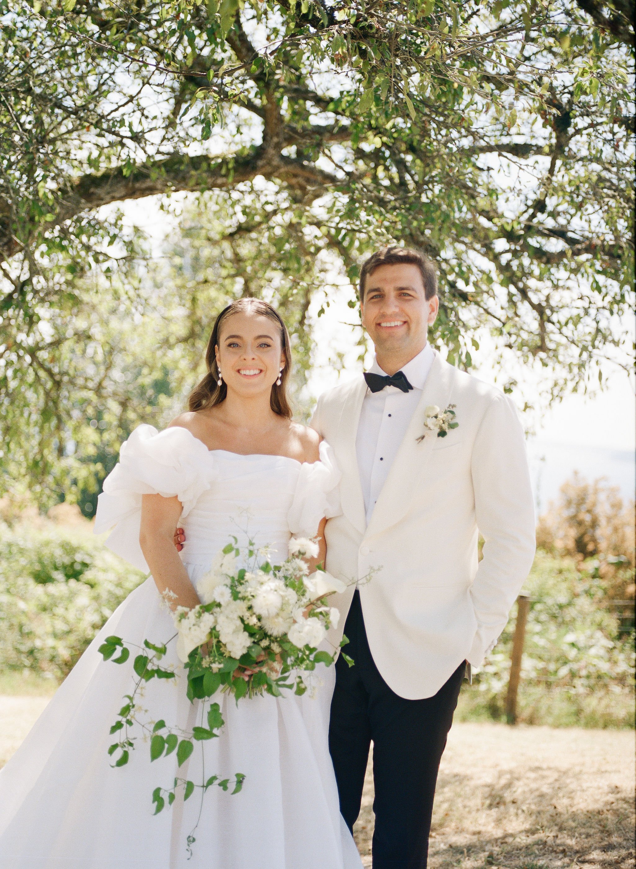 A bride and groom on their wedding day outdoors, smiling, standing close under a large tree with green leaves, sunlight filtering through.
Makeup Katya
Hair Meghhann
Venue Admiral's house
Planner Amber Sooter
Photographer Juliet and Liz