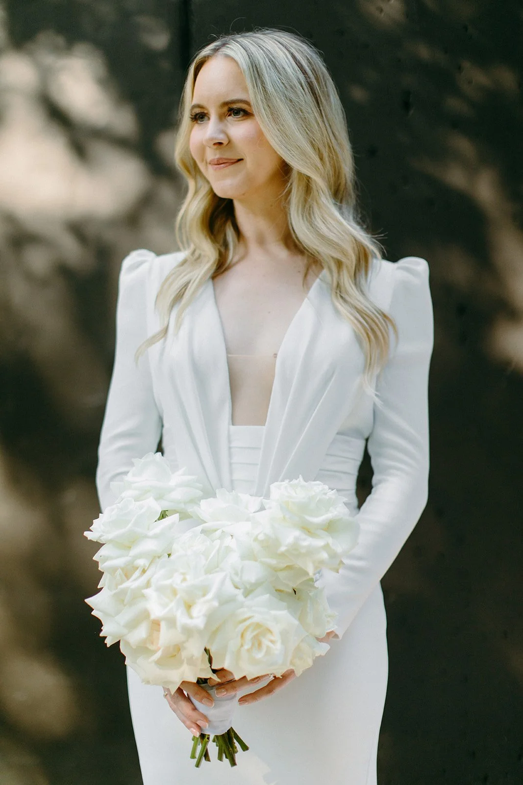 A woman in a white dress holding a bouquet of white roses and lilies.