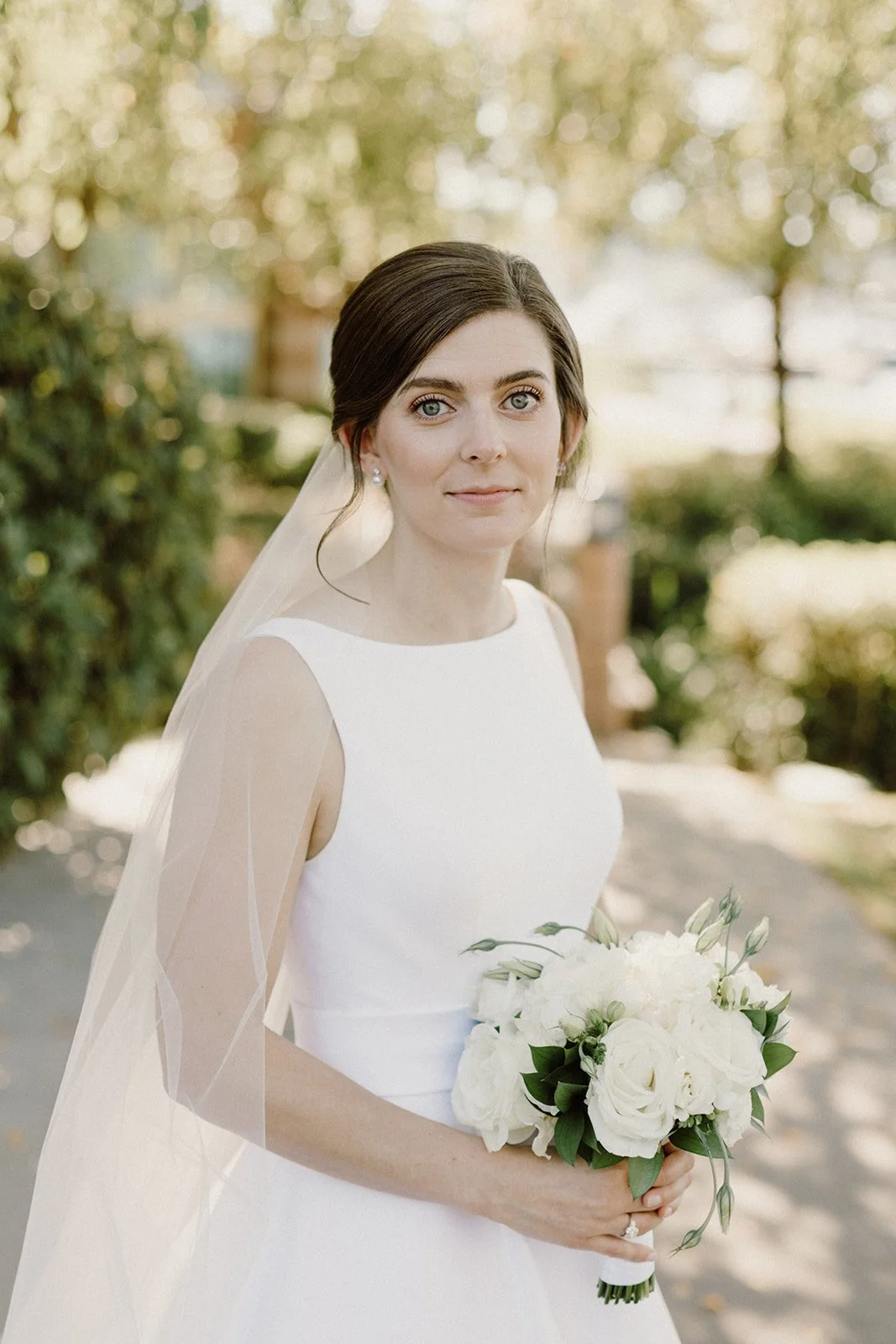 A bride in a white wedding dress holding a bouquet of white roses outdoors on a sunny day.