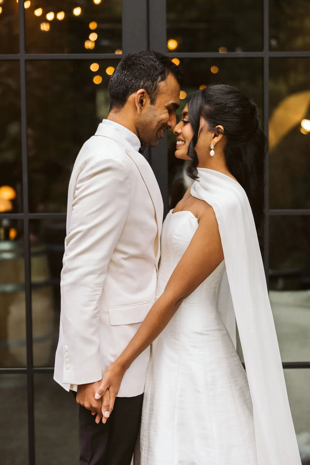 A bride and groom standing close together, touching foreheads and holding hands, in front of a large window with warm lights outside.
Makeup Karla, Bridal Beauty Agency
Hair Lindsey Bridal Beauty Agency
Venue: JM Cellars
Planning & Design: Audrey Gra