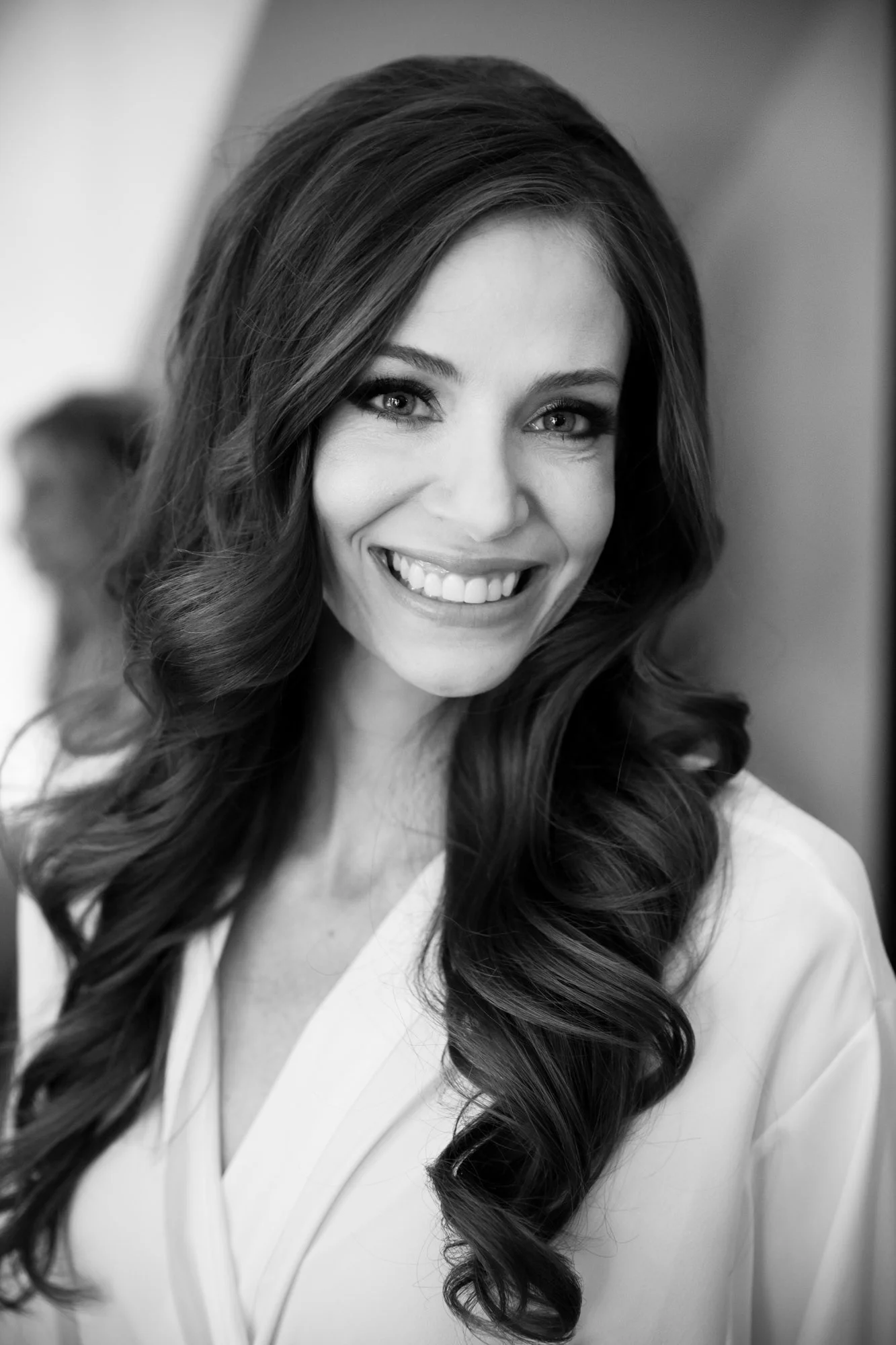 Black and white portrait of a smiling woman with long wavy hair, wearing a light-colored top, looking at the camera.