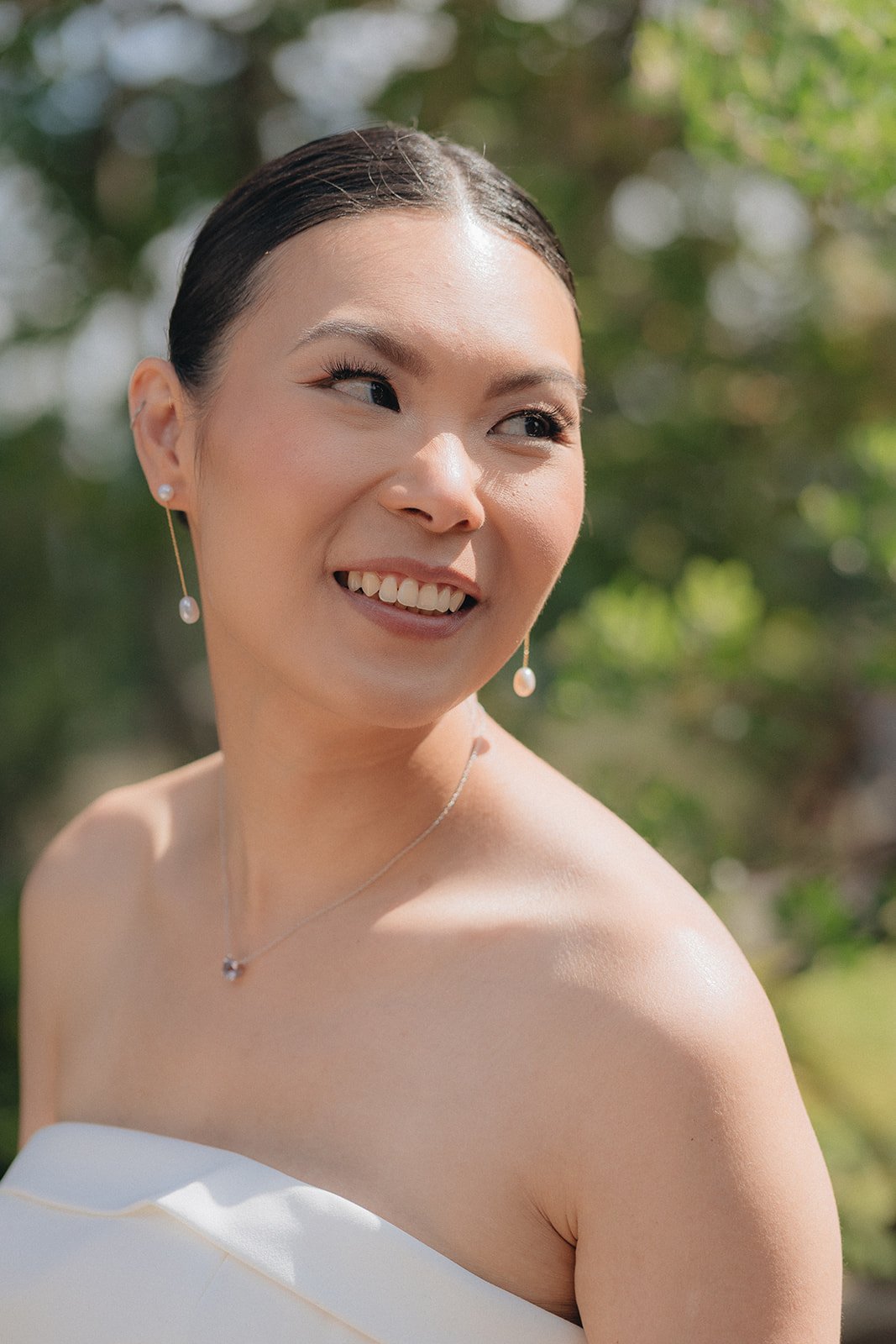 A smiling woman with dark hair styled back, wearing pearl earrings and a necklace, outside with blurred green foliage in the background.
Karla makeup, Meghann hair
Photographer Kris Ladera 
Planner Lyndsay A Renee weddings
Venuew UW Center for Urban 