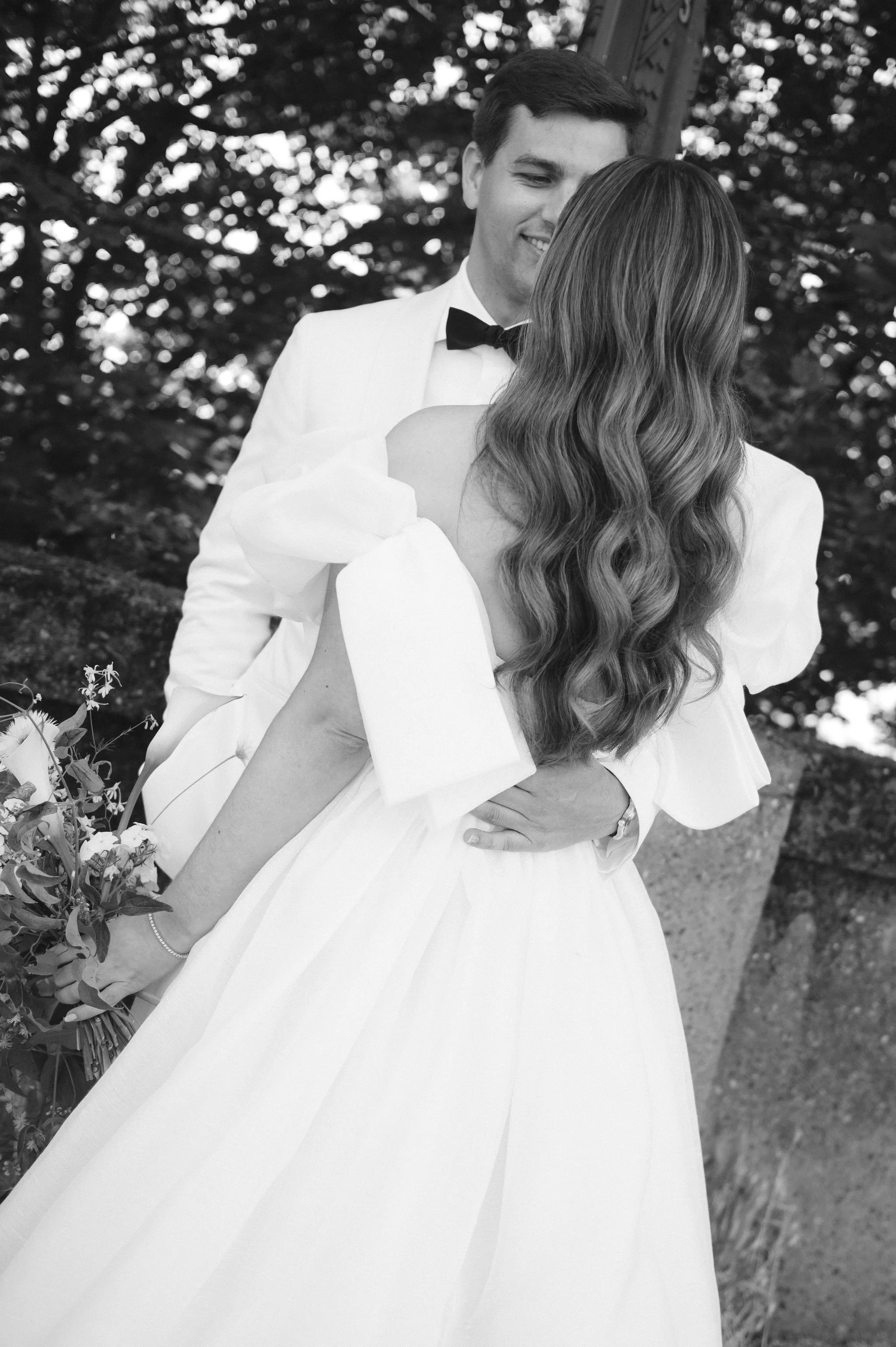 A black and white photo of a man in a tuxedo gently holding a woman in a wedding dress, both smiling, in an outdoor setting with trees in the background.
Makeup Katya
Hair Meghhann
Venue Admiral's house
Planner Amber Sooter
Photographer Juliet and Li