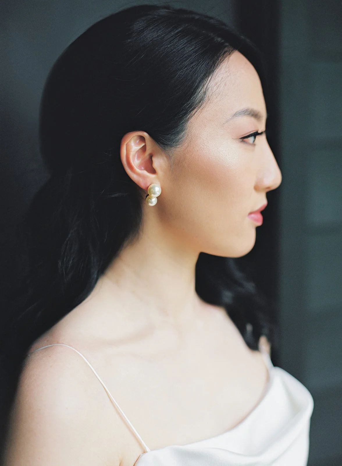 Profile view of a woman with long black hair, wearing pearl earrings and a white off-shoulder dress.
Makeup and hair Stace, Bridal Beauty Agency
Photographer Tetiana Photography
Venue JM Cellars
Planner Celebrate with Caroline
